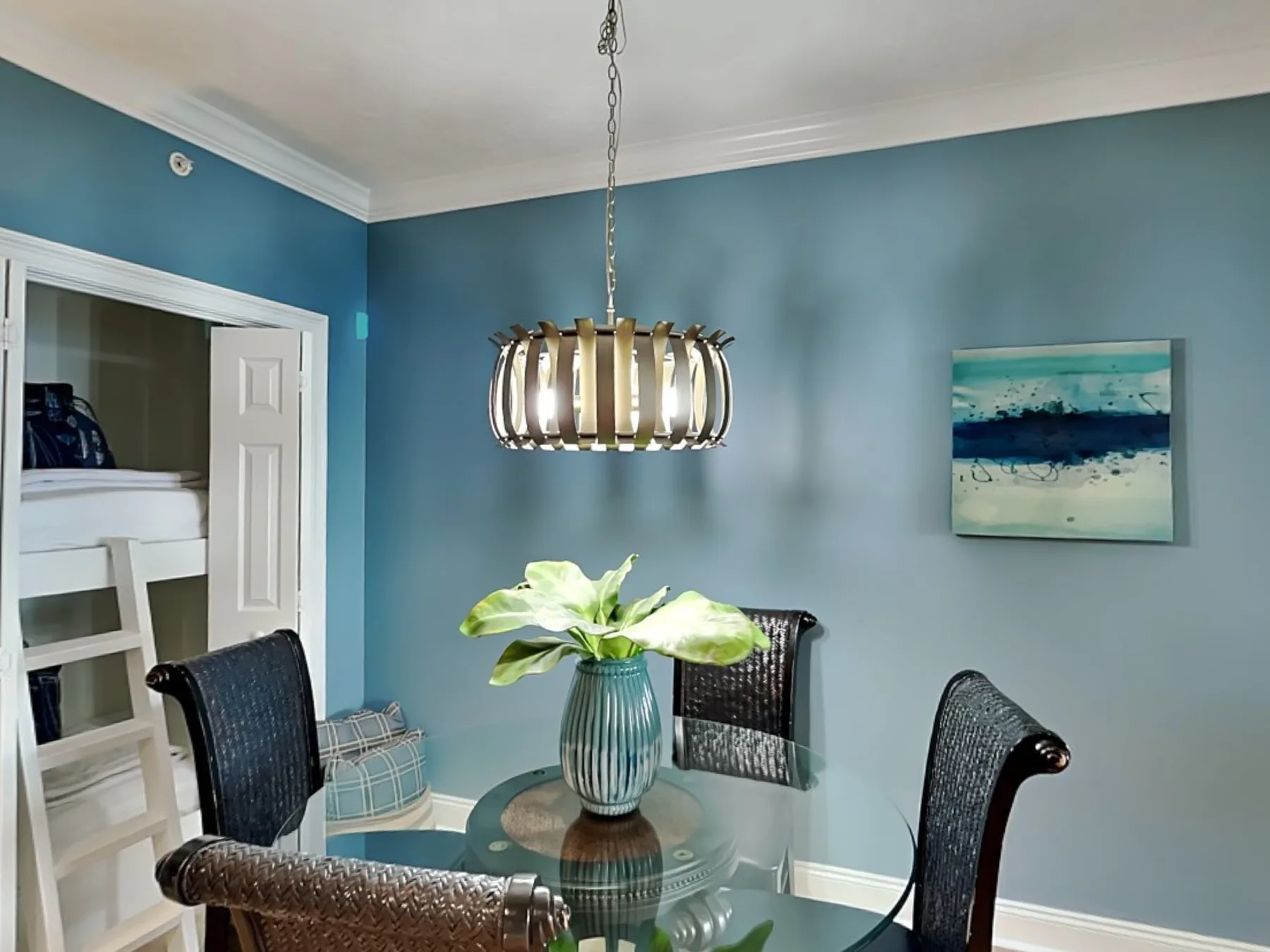 A dining area with a round glass table, dark seating, and a hanging light.