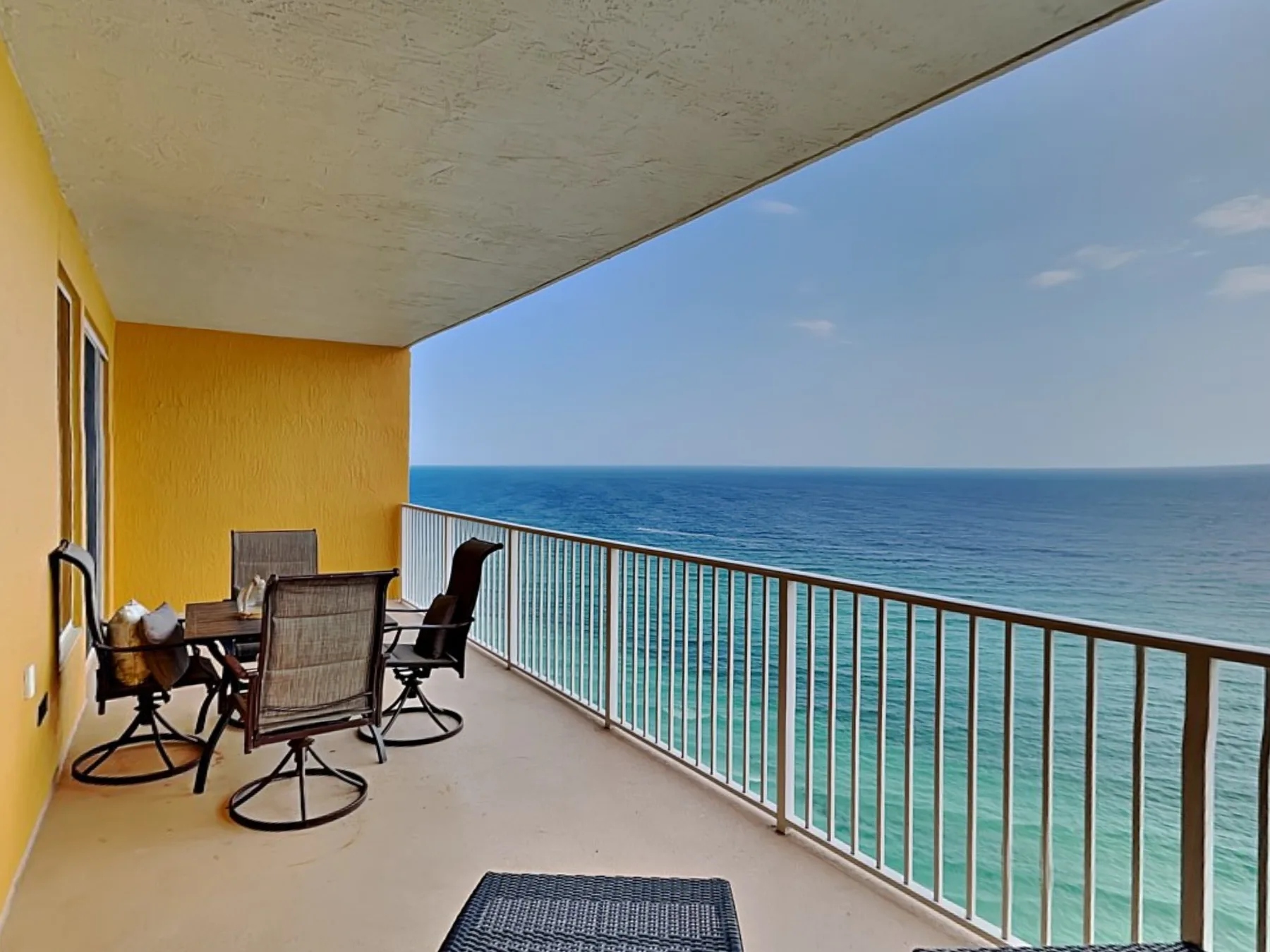 A covered balcony overlooks the ocean, with outdoor seating and a table.