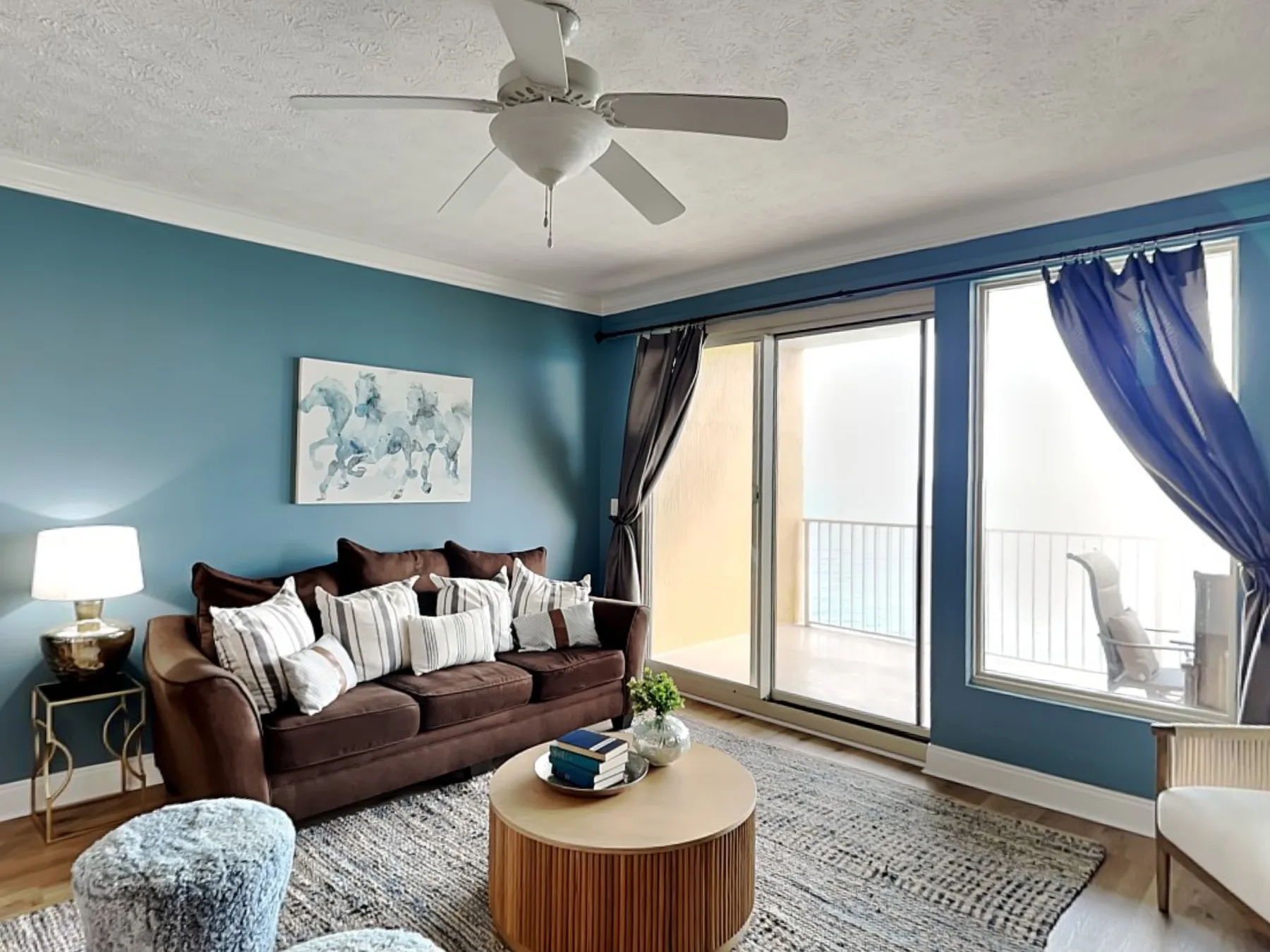 A living room with seating, a coffee table, and large windows opening onto a balcony.
