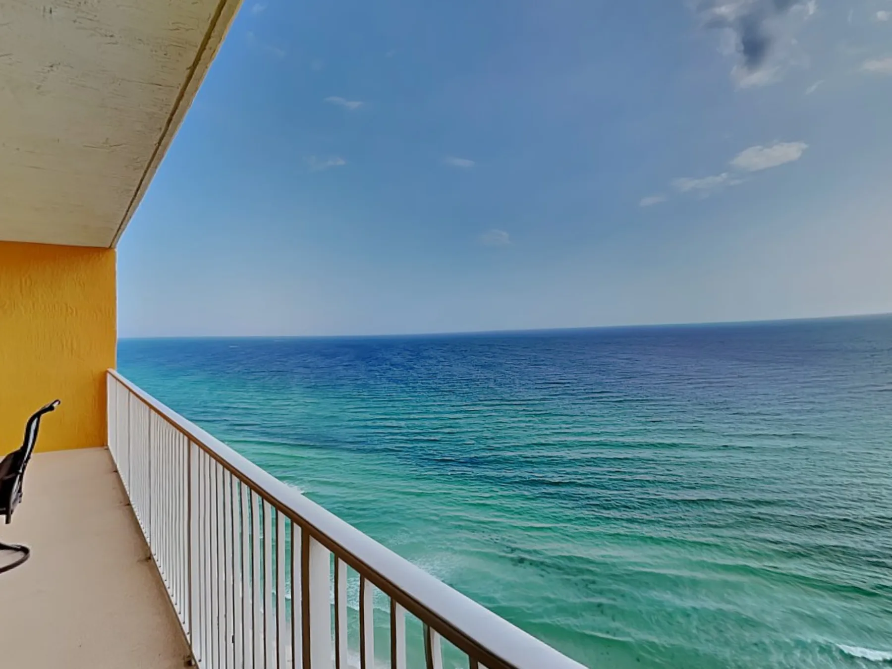 A balcony overlooks the turquoise ocean beneath a partly cloudy sky.