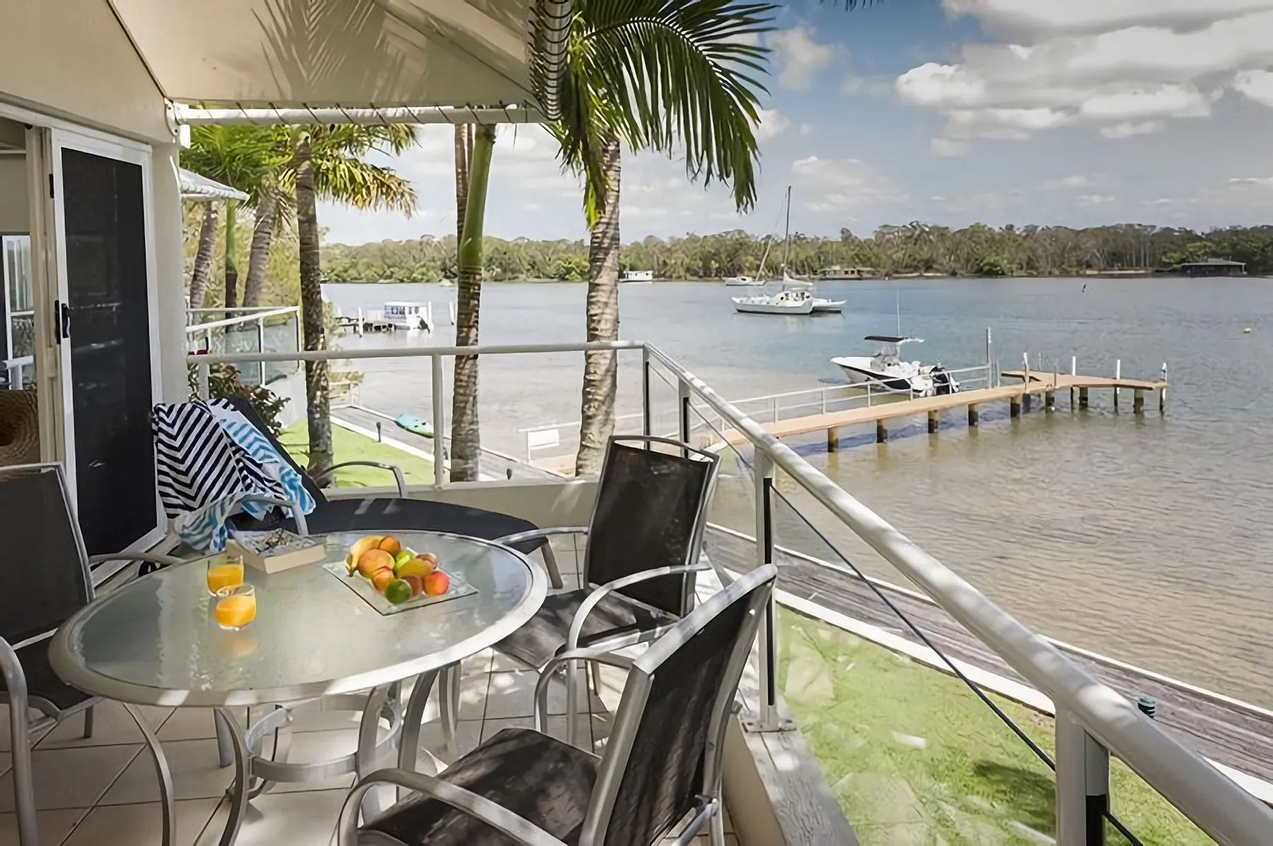 Un balcón junto al río tiene una mesa de comedor de vidrio y vistas al agua.