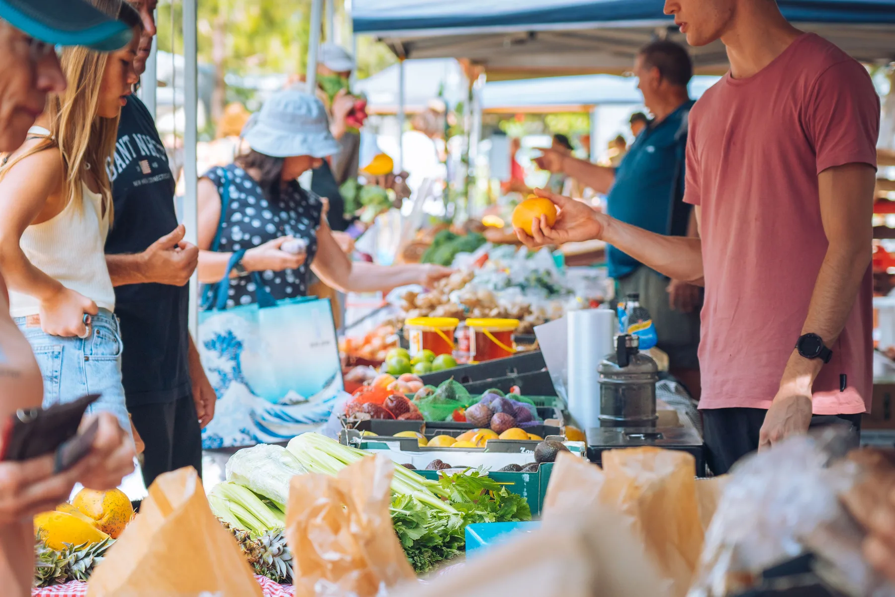 Varias personas compran productos frescos en un puesto de mercado al aire libre.