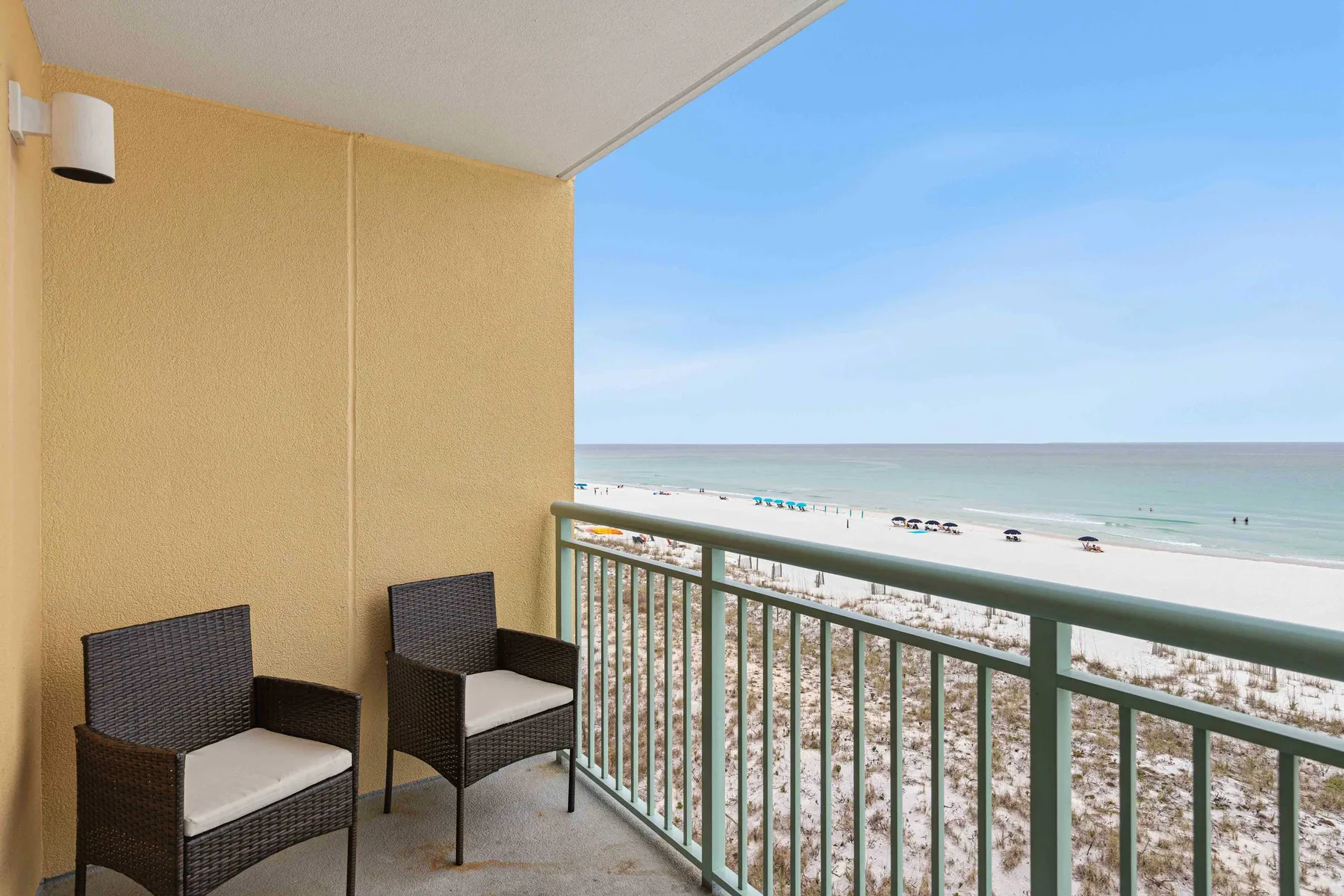 A balcony with seating overlooks a sandy beach and the ocean.