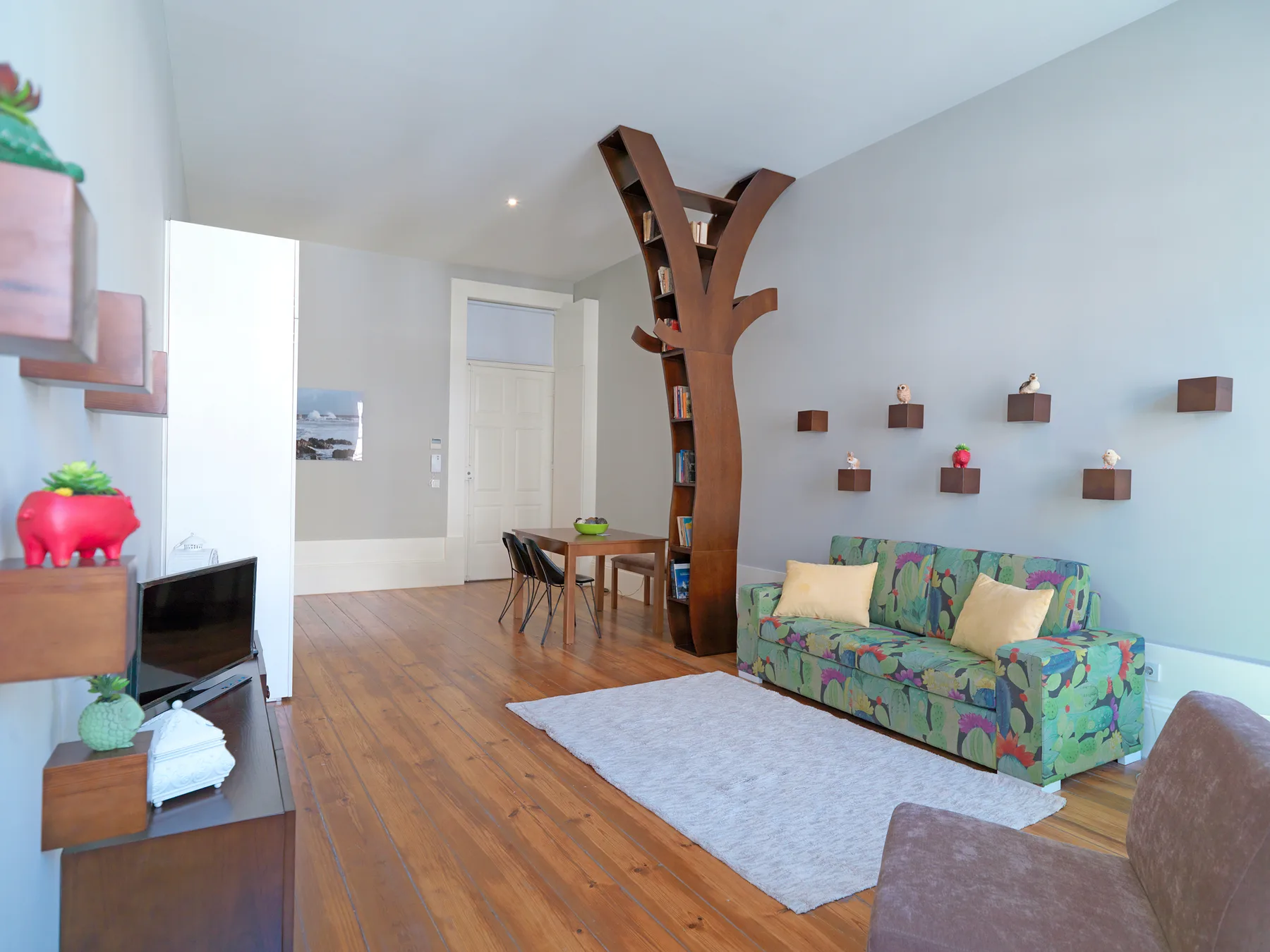 Living room with a colorful sofa, wooden shelving, and a dining area.