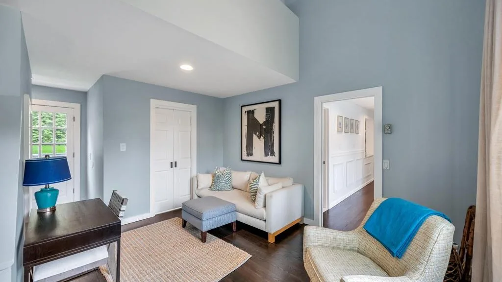 A living room with light seating, a blue accent chair, and a large area rug.
