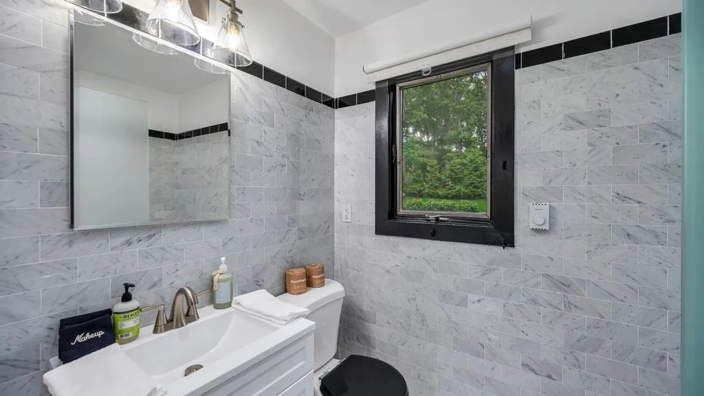 A tiled bathroom with a sink, mirror, and window.