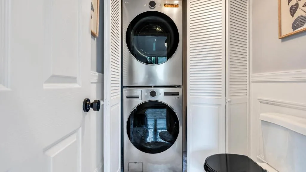 A laundry area with a stacked washer and dryer behind louvered doors.