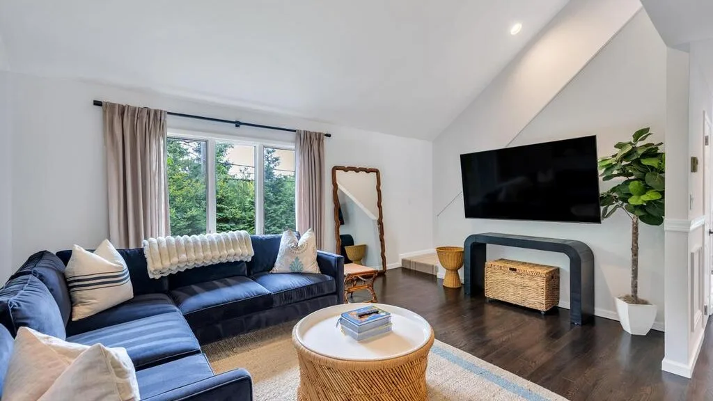 Una sala de estar con asientos azules, un televisor y una ventana grande.