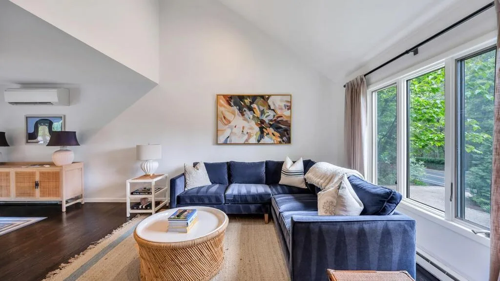 A bright living room with sectional seating and large windows overlooking greenery.