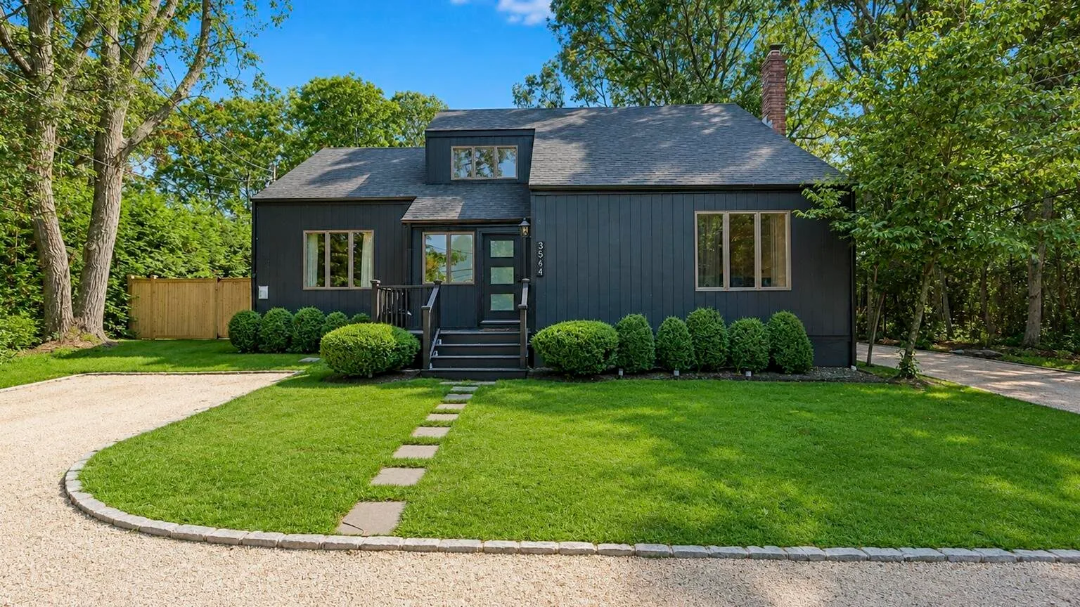 A dark-sided house stands behind a green lawn and stepping-stone path.