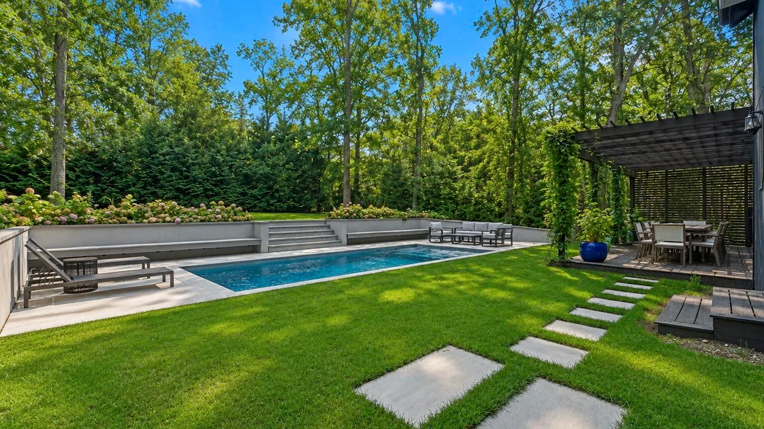 Un jardín cuidado con piscina, césped y una zona de asientos a la sombra.