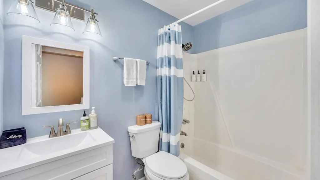 A bathroom with a white sink, mirror, toilet, and shower curtain.