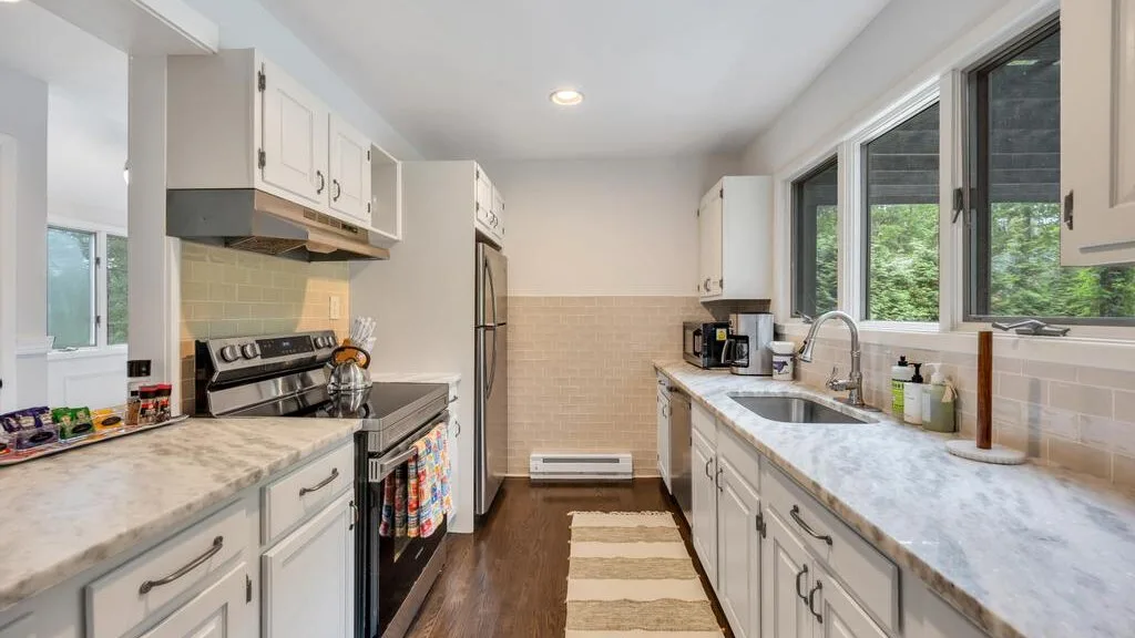A bright kitchen with white cabinets, long counters, and large windows.