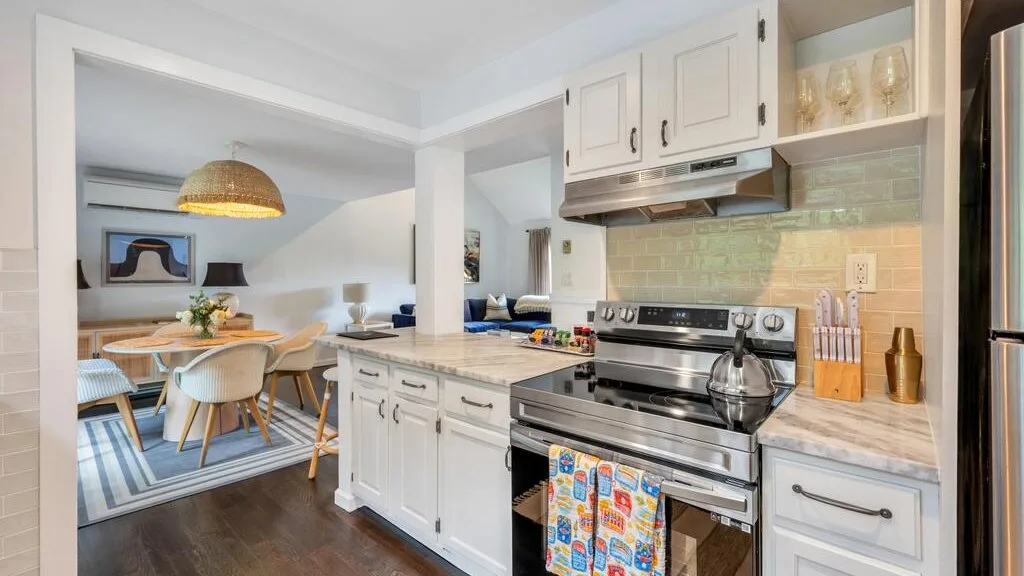 A bright kitchen with white cabinetry, a stainless steel range, and a dining area.