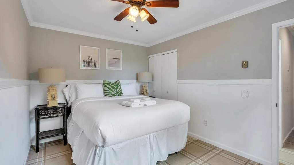 A bright bedroom with a neatly made bed and framed artwork on the wall.