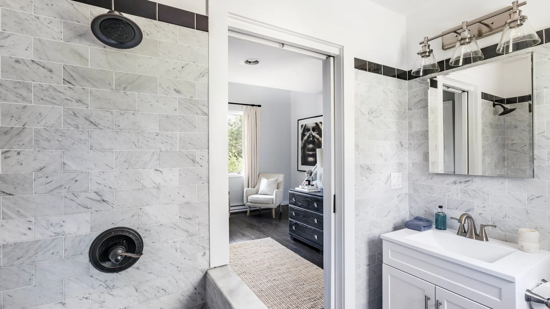 A bright bathroom with a marble-tiled shower and a white vanity.