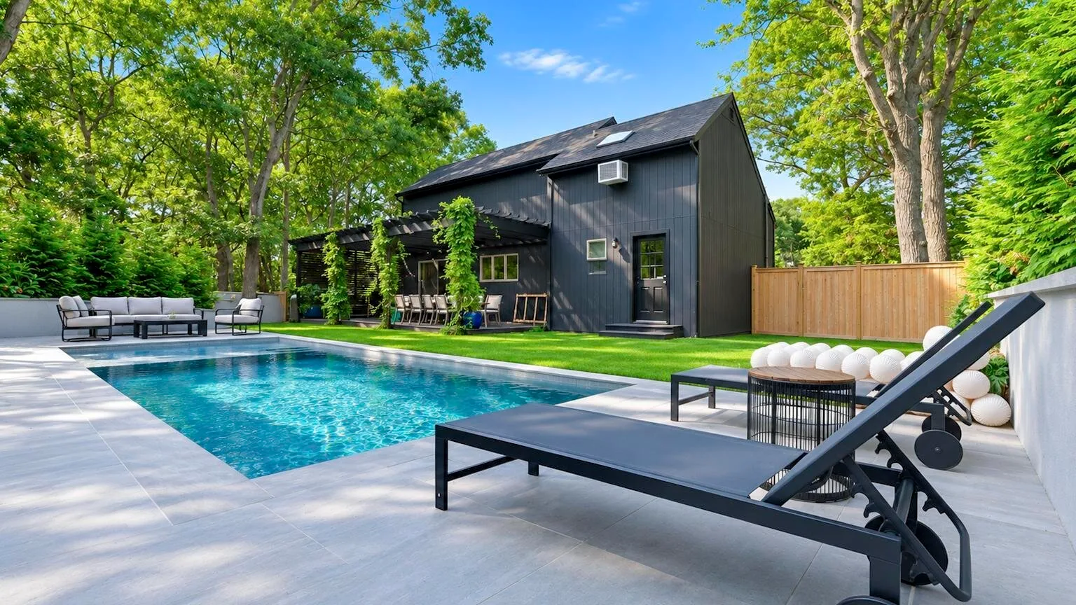 A swimming pool and patio beside a dark house, surrounded by trees.