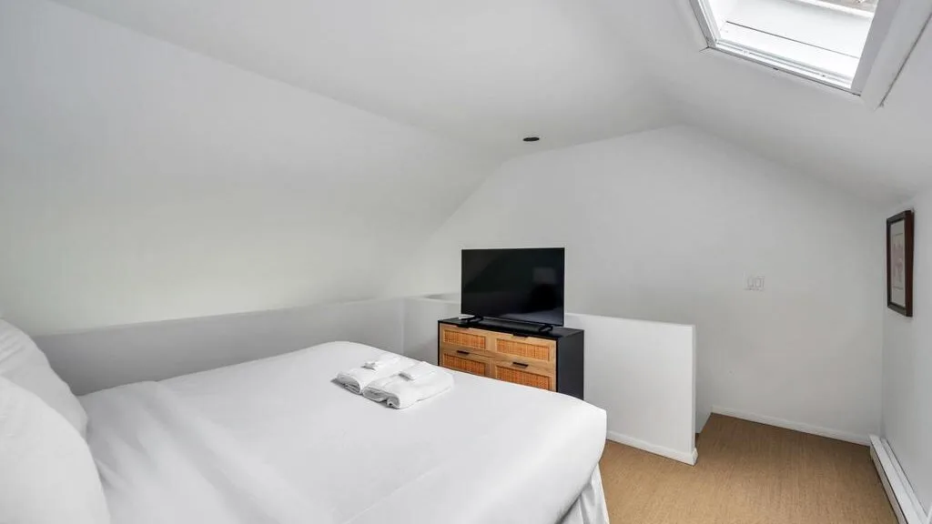 A bright bedroom with a bed, television, and skylight.