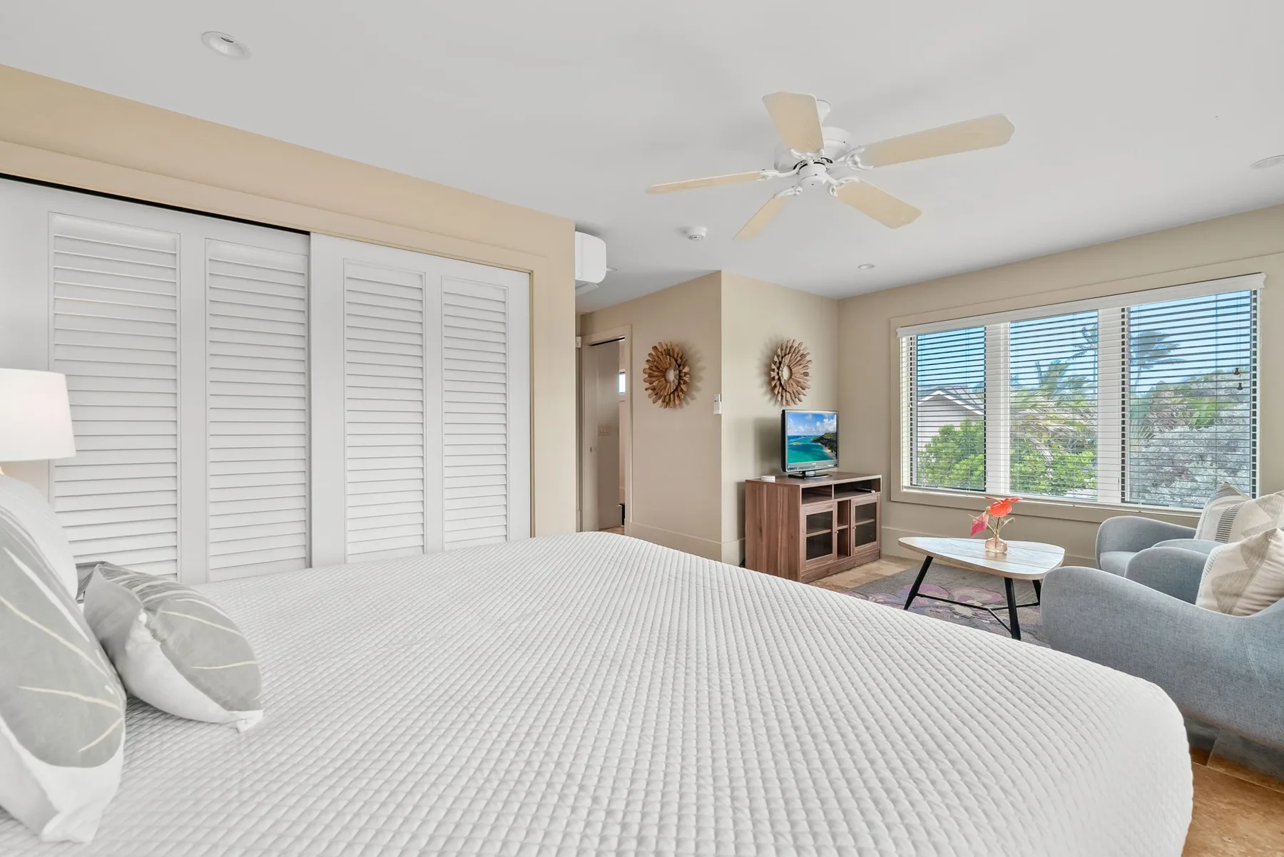 A bedroom with a large bed, seating area, and windows with blinds.