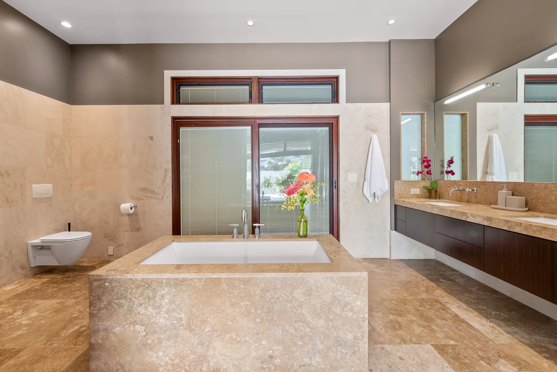 A spacious bathroom with a bathtub, wall-mounted sink, and large windows.