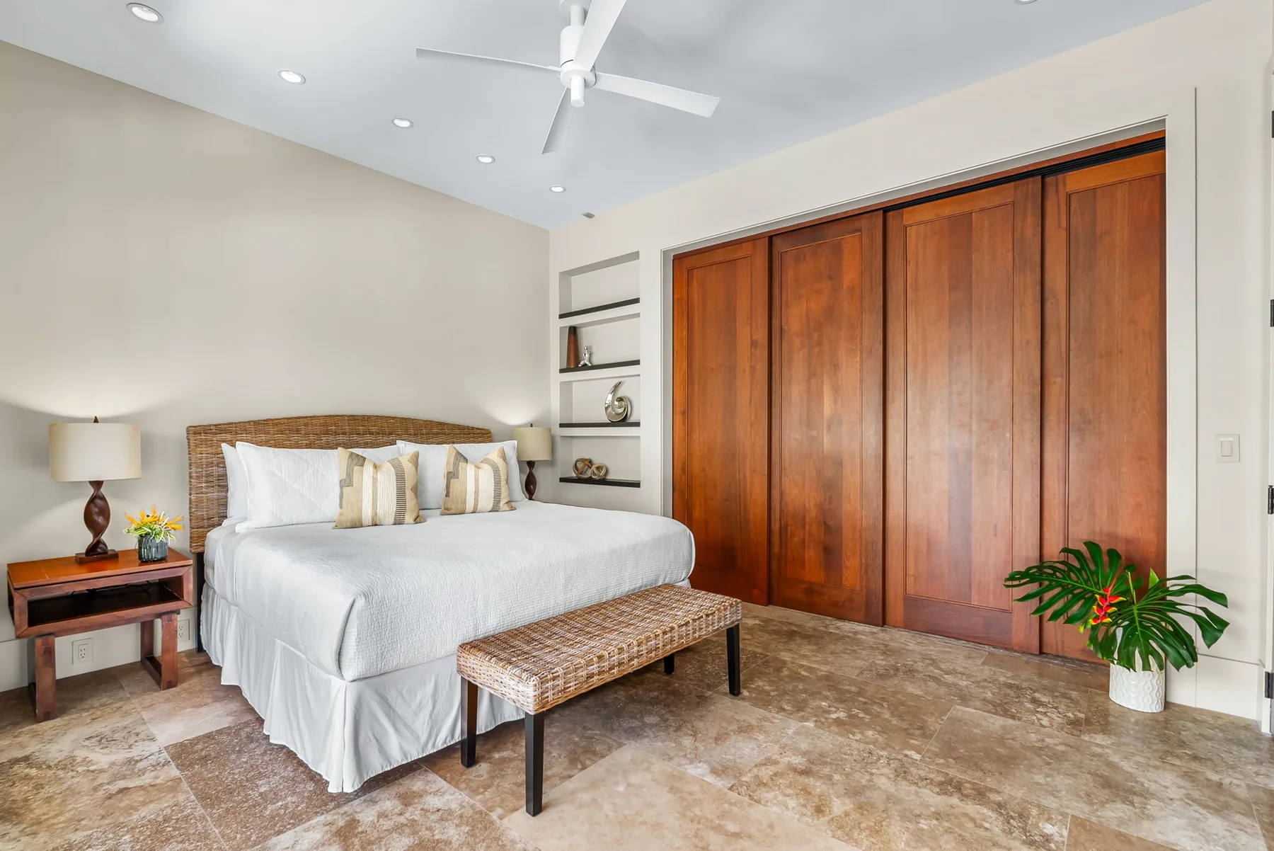 A bedroom with a neatly made bed, a wooden wardrobe, and a woven bench.