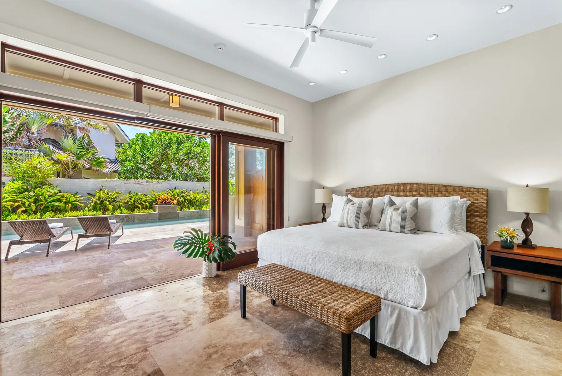 A bedroom with a white bed, woven bench, and sliding glass doors opening to a patio.