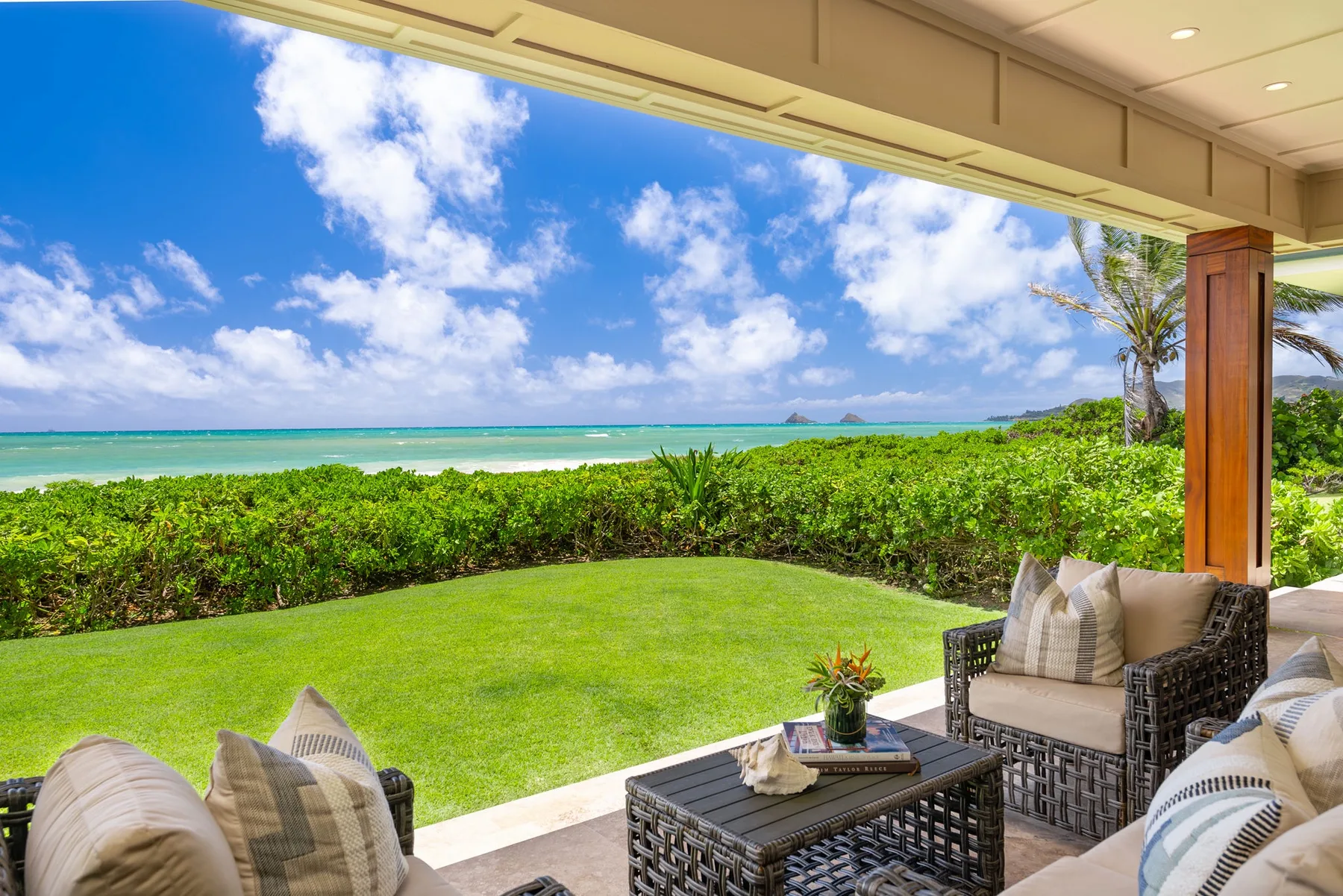 A covered outdoor patio with seating overlooks a green lawn and ocean.
