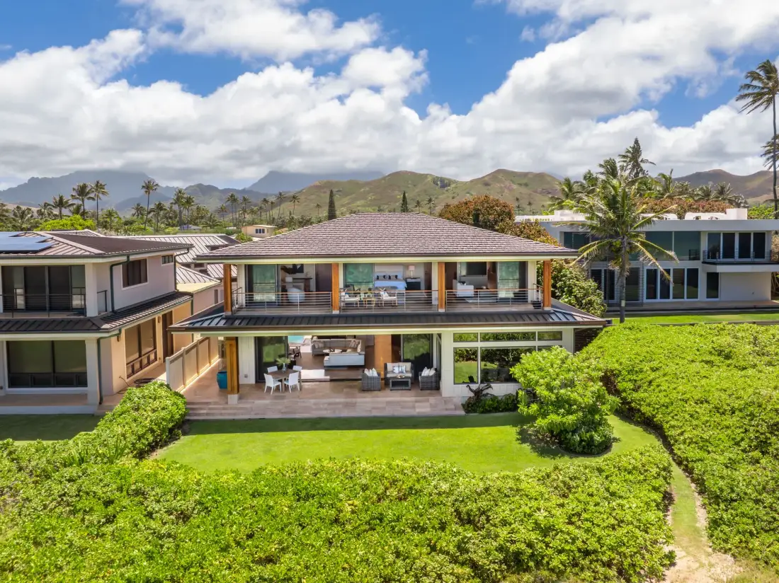 A two-story house overlooks a green lawn and surrounding hills.