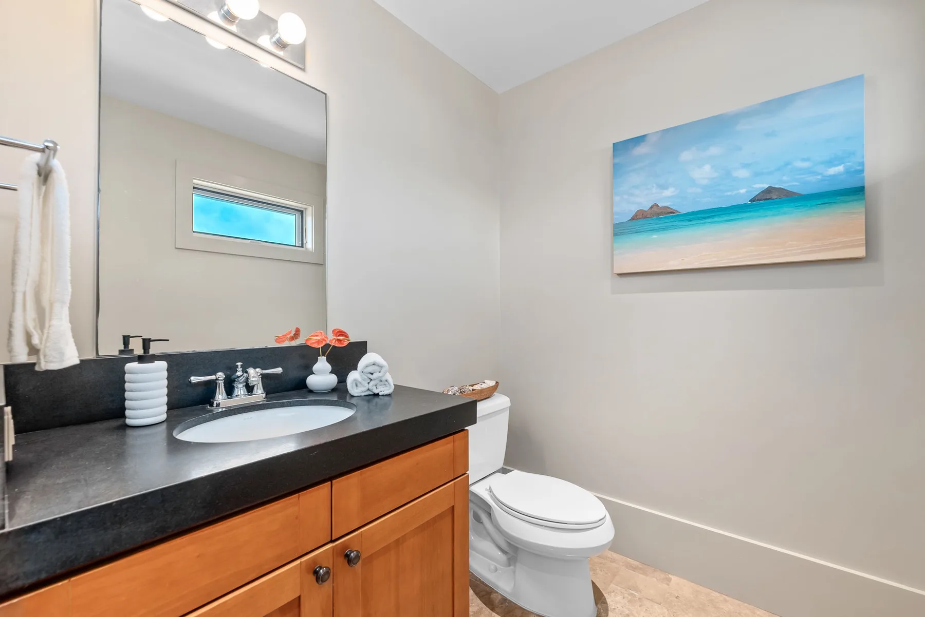 A bathroom with a vanity, sink, toilet, and beach scene artwork on the wall.