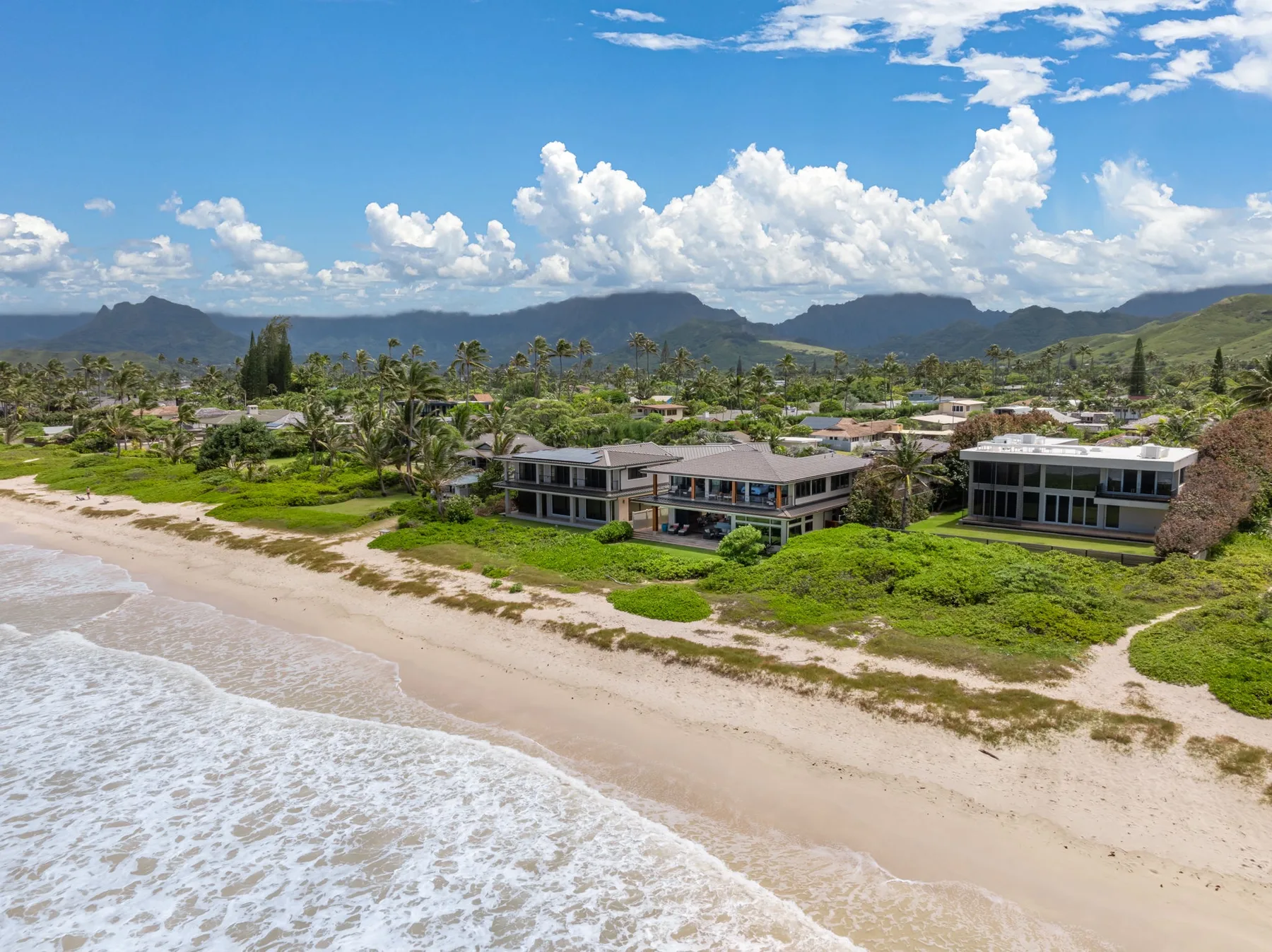 Aerial view of a sandy beach and beachfront buildings beneath a mountain range.