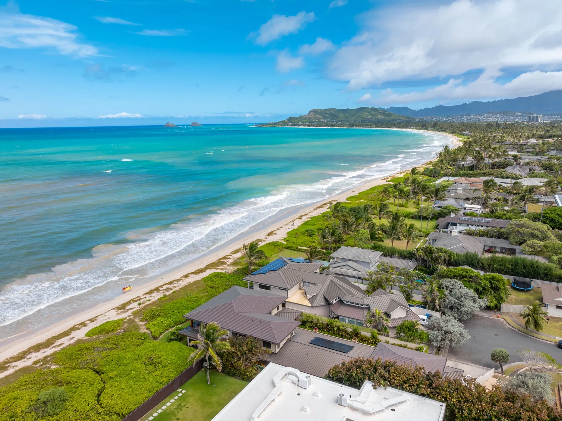 Aerial coastal view of a sandy beach, turquoise water, and nearby homes.