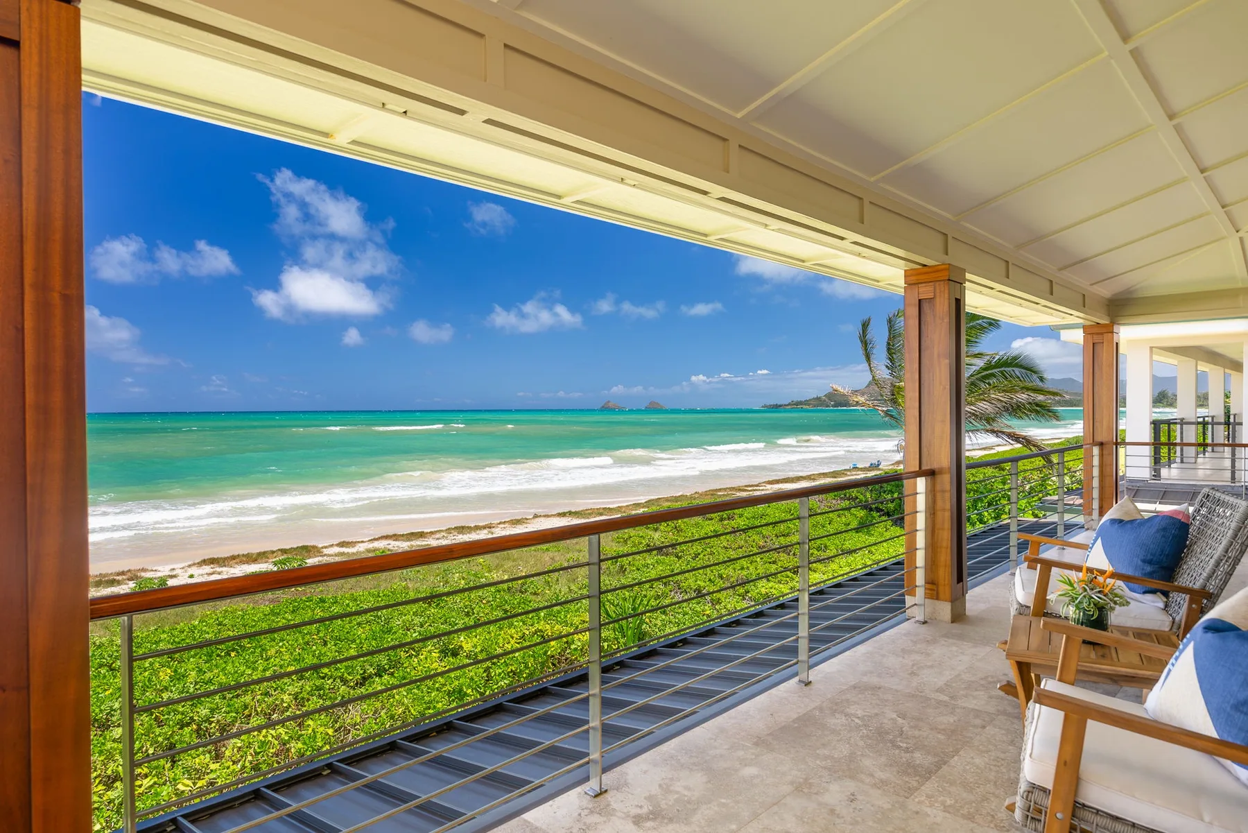 A covered oceanfront balcony overlooks turquoise water and a green shoreline.