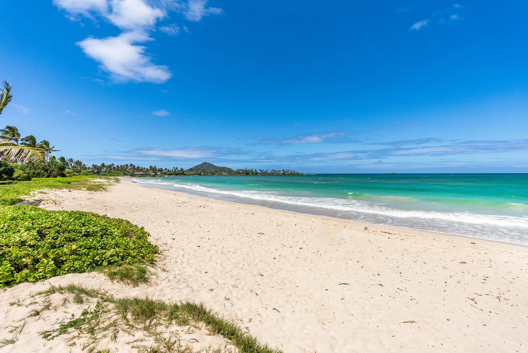 A sandy beach borders turquoise water beneath a wide blue sky.