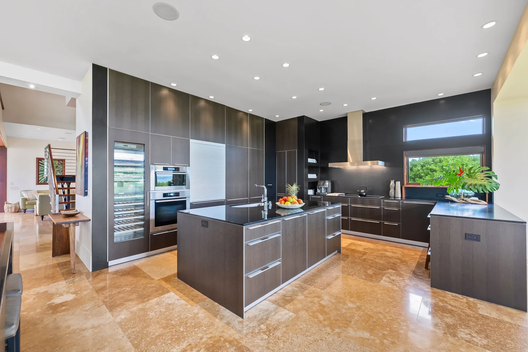A modern kitchen with dark cabinets, a central island, and large windows.