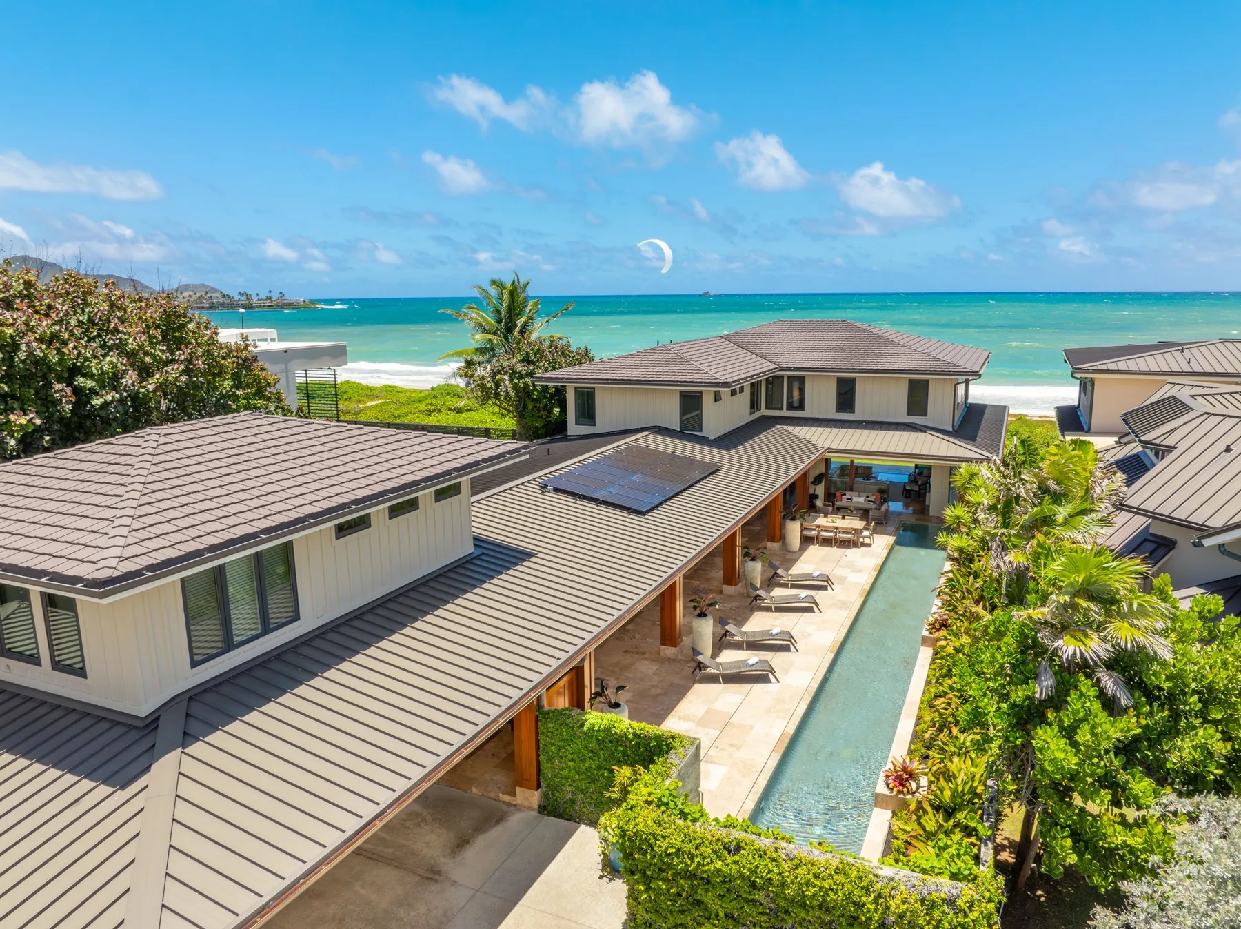 A coastal resort with a long swimming pool, palm trees, and the ocean beyond.