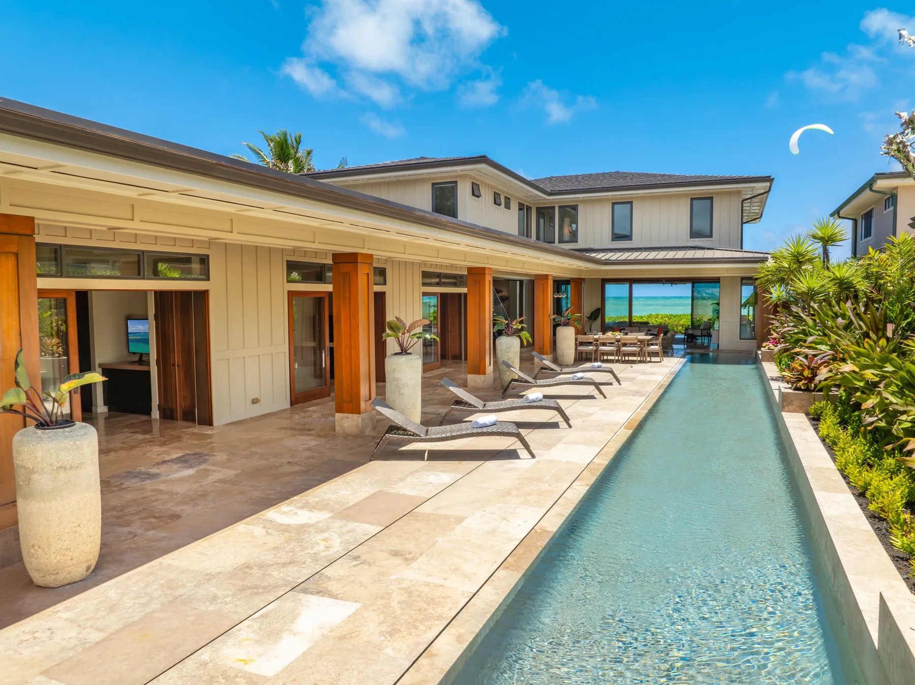 A sunny outdoor pool runs alongside a covered patio with lounge seating.