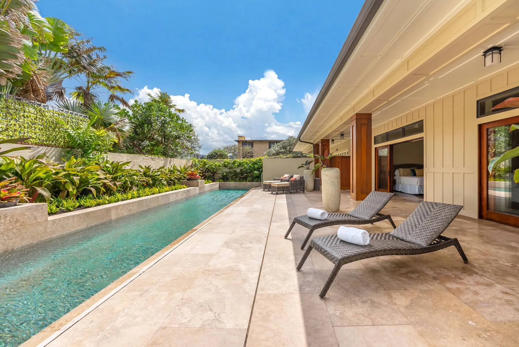 A poolside patio with lounge seating beside a long swimming pool.