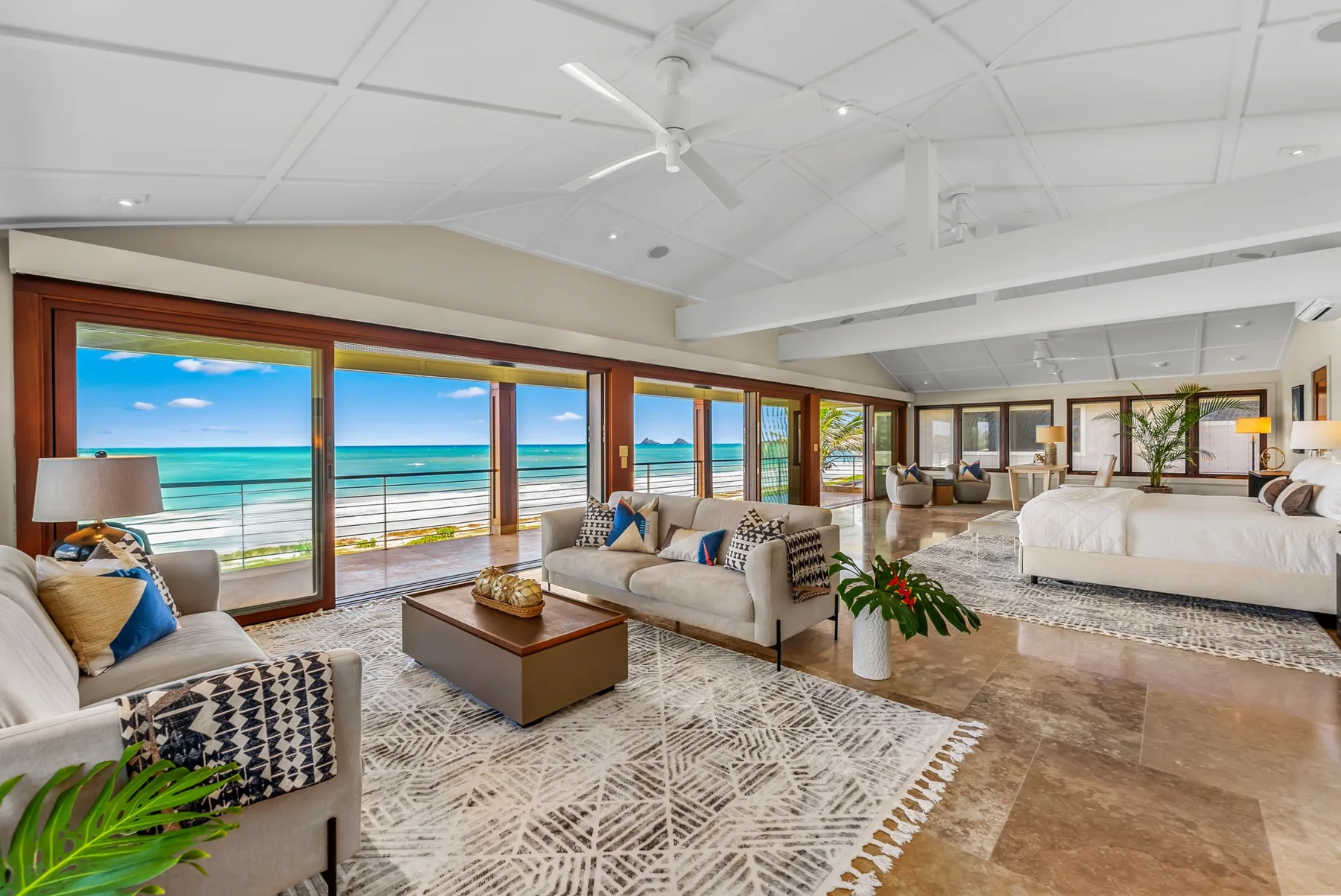 A bright living area with seating, a coffee table, and large windows overlooking the ocean.