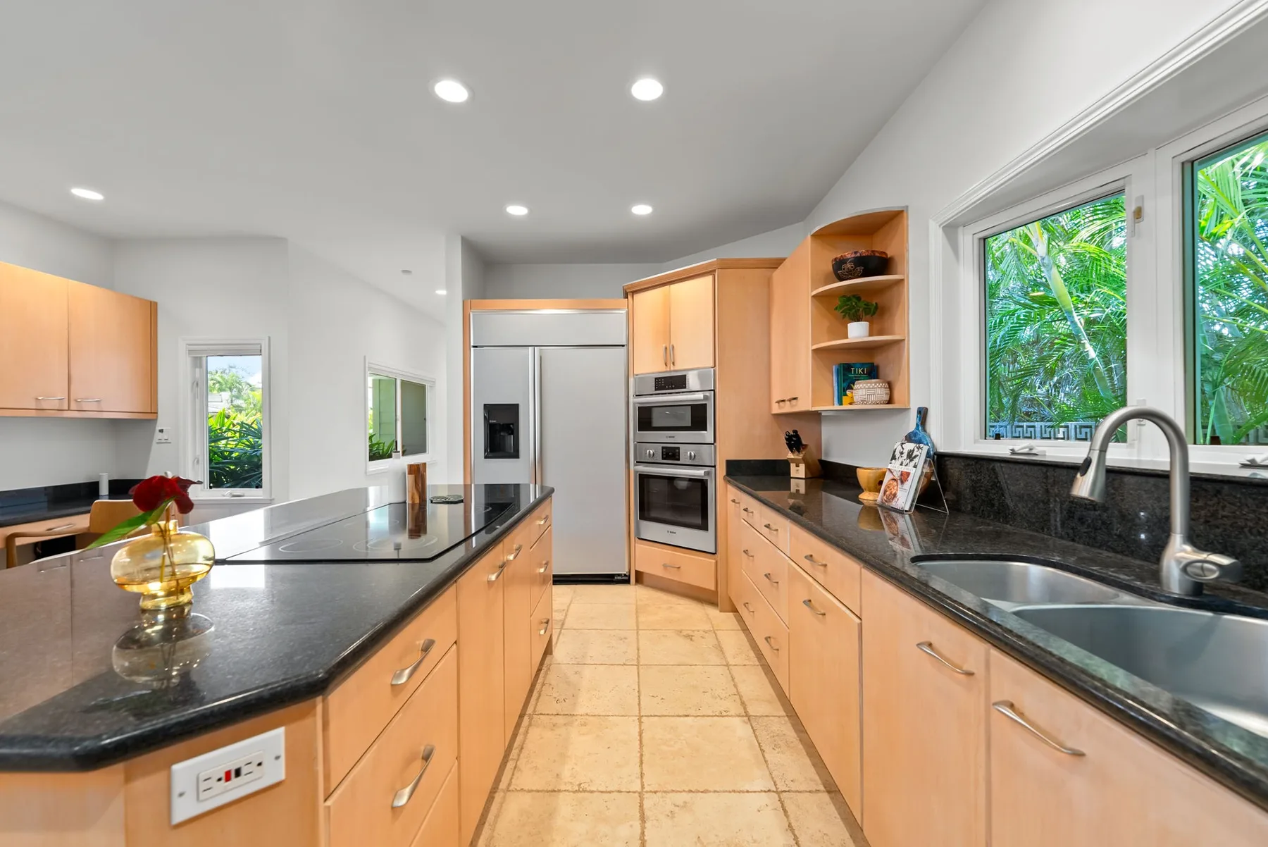 Una cocina luminosa con gabinetes de madera, encimeras oscuras y un refrigerador de acero inoxidable.