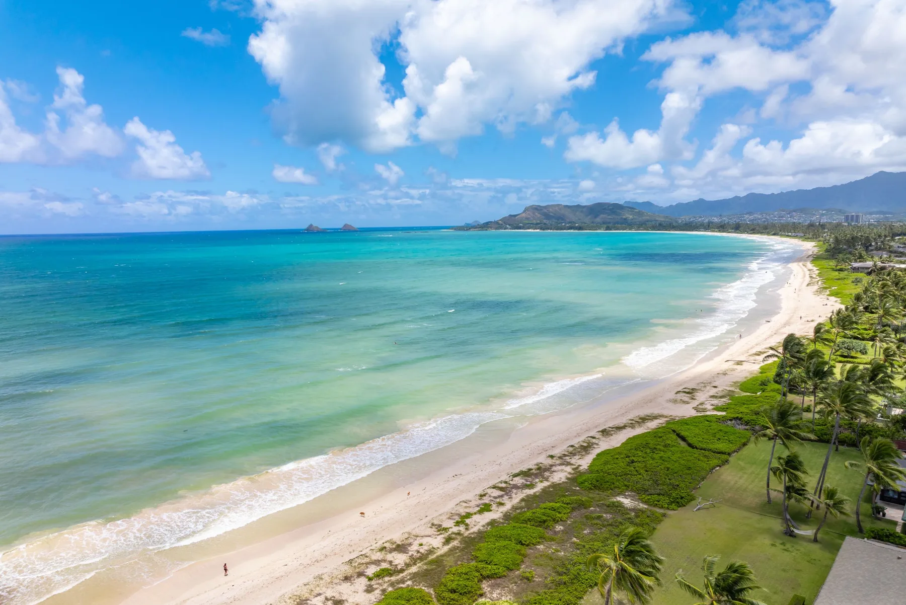 Una playa tropical bordea aguas turquesas, con colinas verdes a lo lejos.