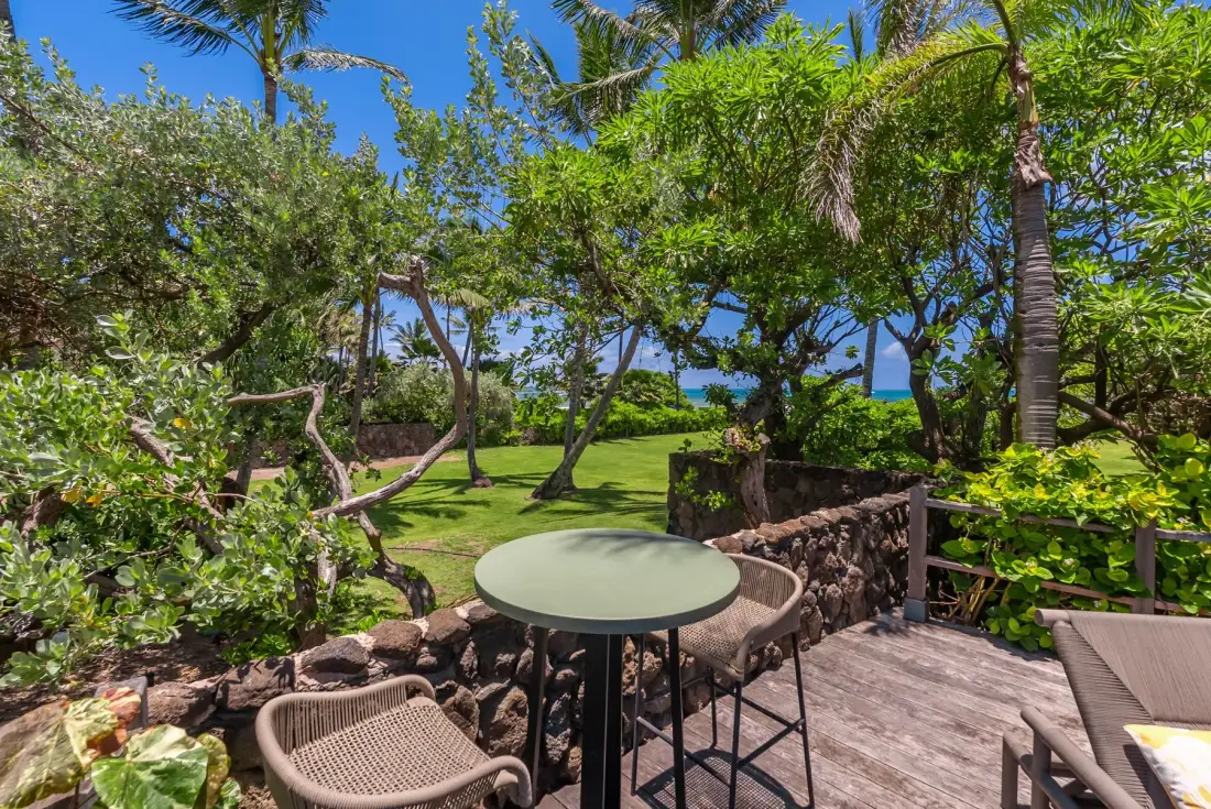 Un patio exterior sombreado con una mesa y asientos da a un jardín frondoso.