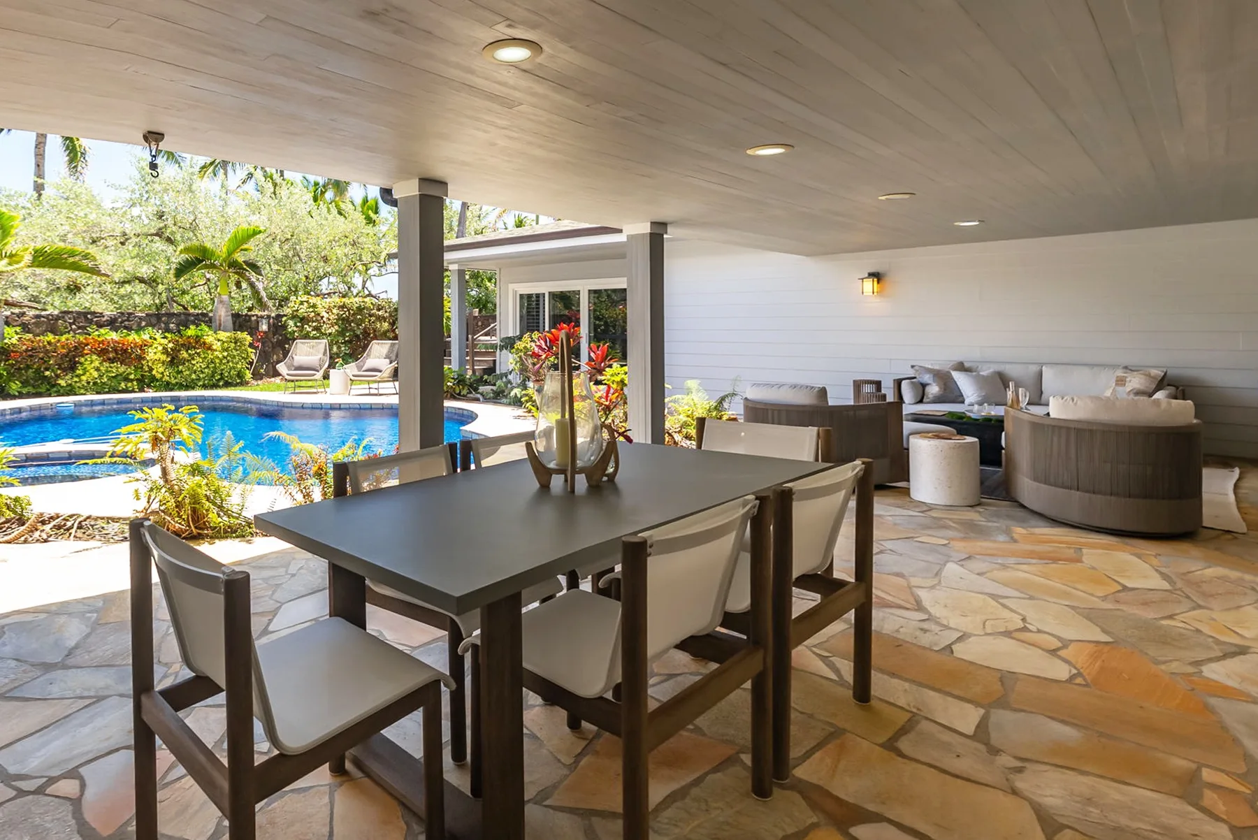 A covered outdoor dining area overlooks a swimming pool and landscaped garden.