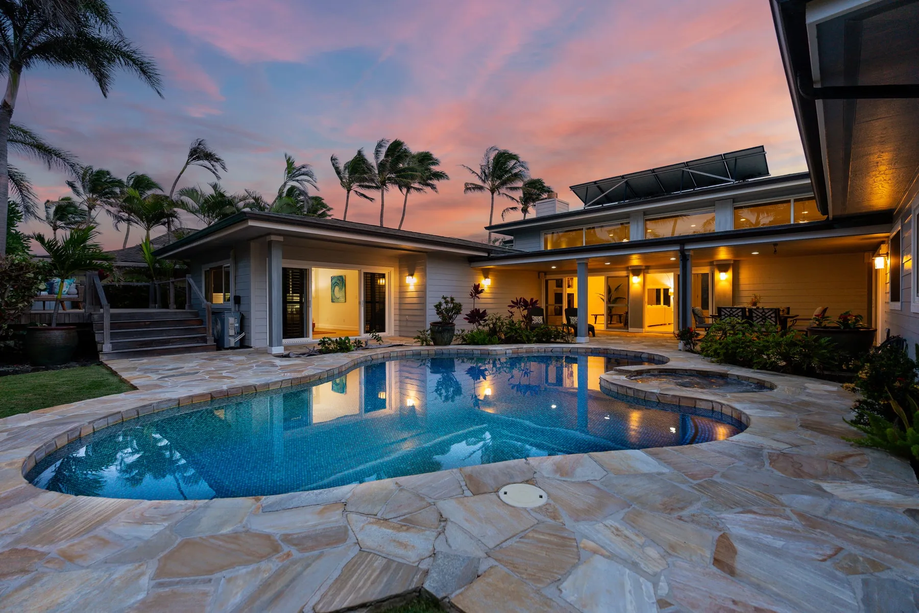 Una piscina y un patio pavimentado están frente a una casa moderna al atardecer.