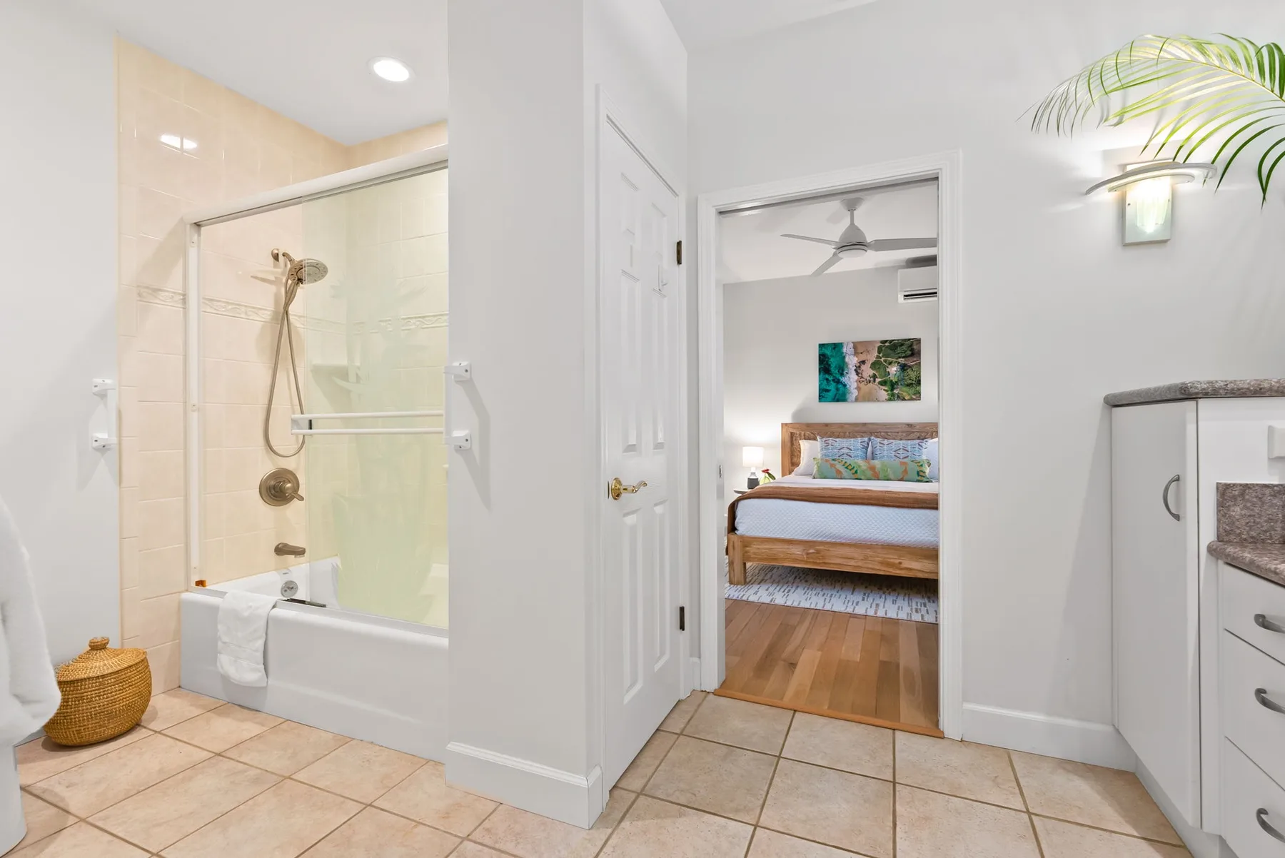 Un baño se abre a un dormitorio con una cama de madera y un ventilador de techo.