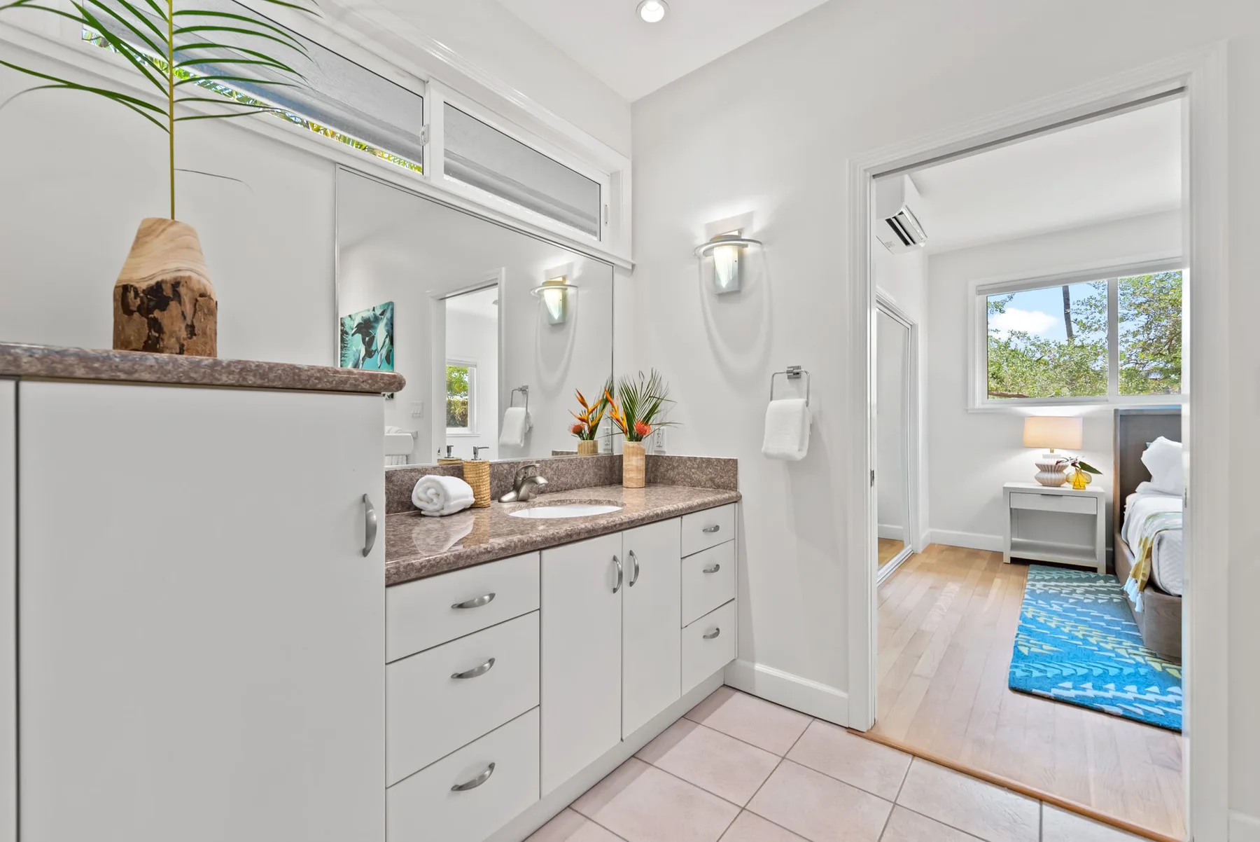 Un baño luminoso con lavabo y espejo se abre a un dormitorio.