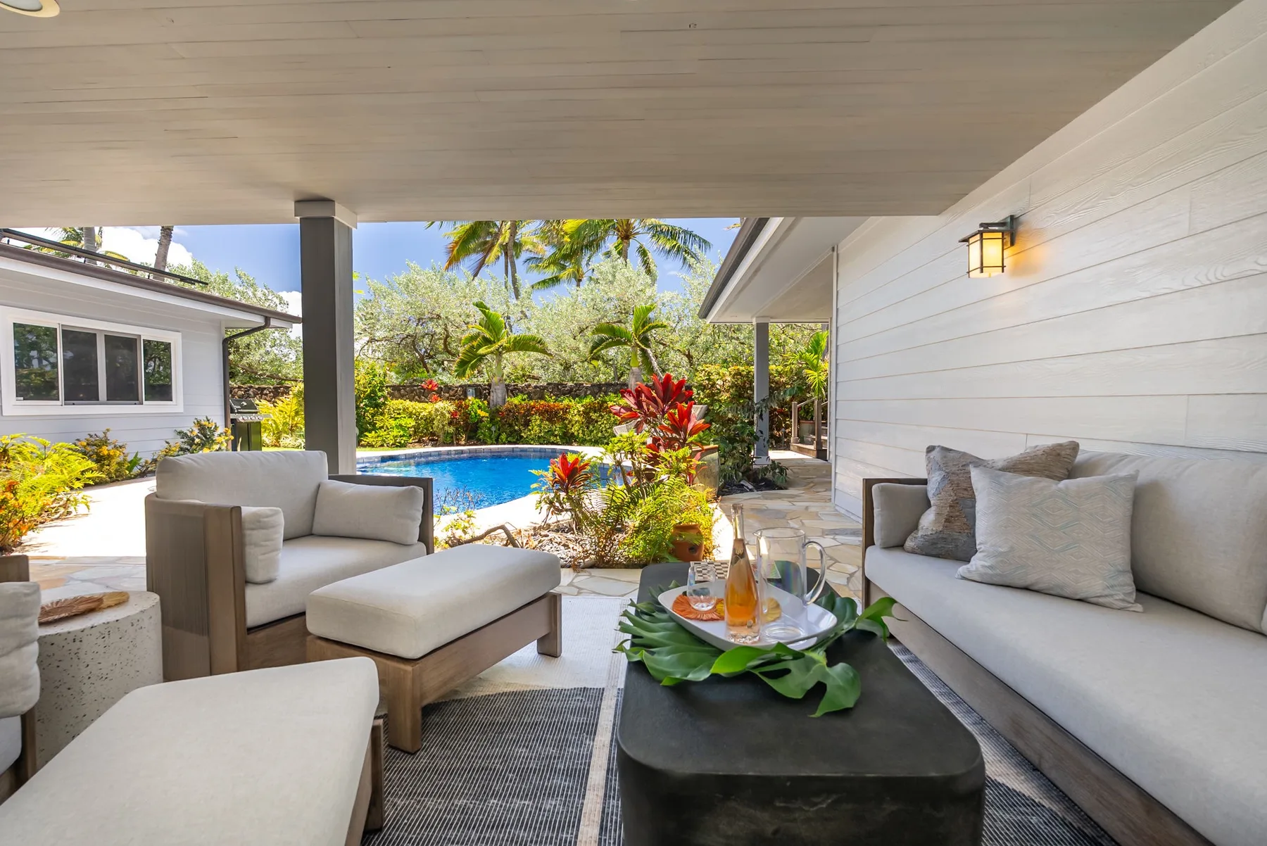 A covered outdoor seating area overlooks a swimming pool and tropical garden.