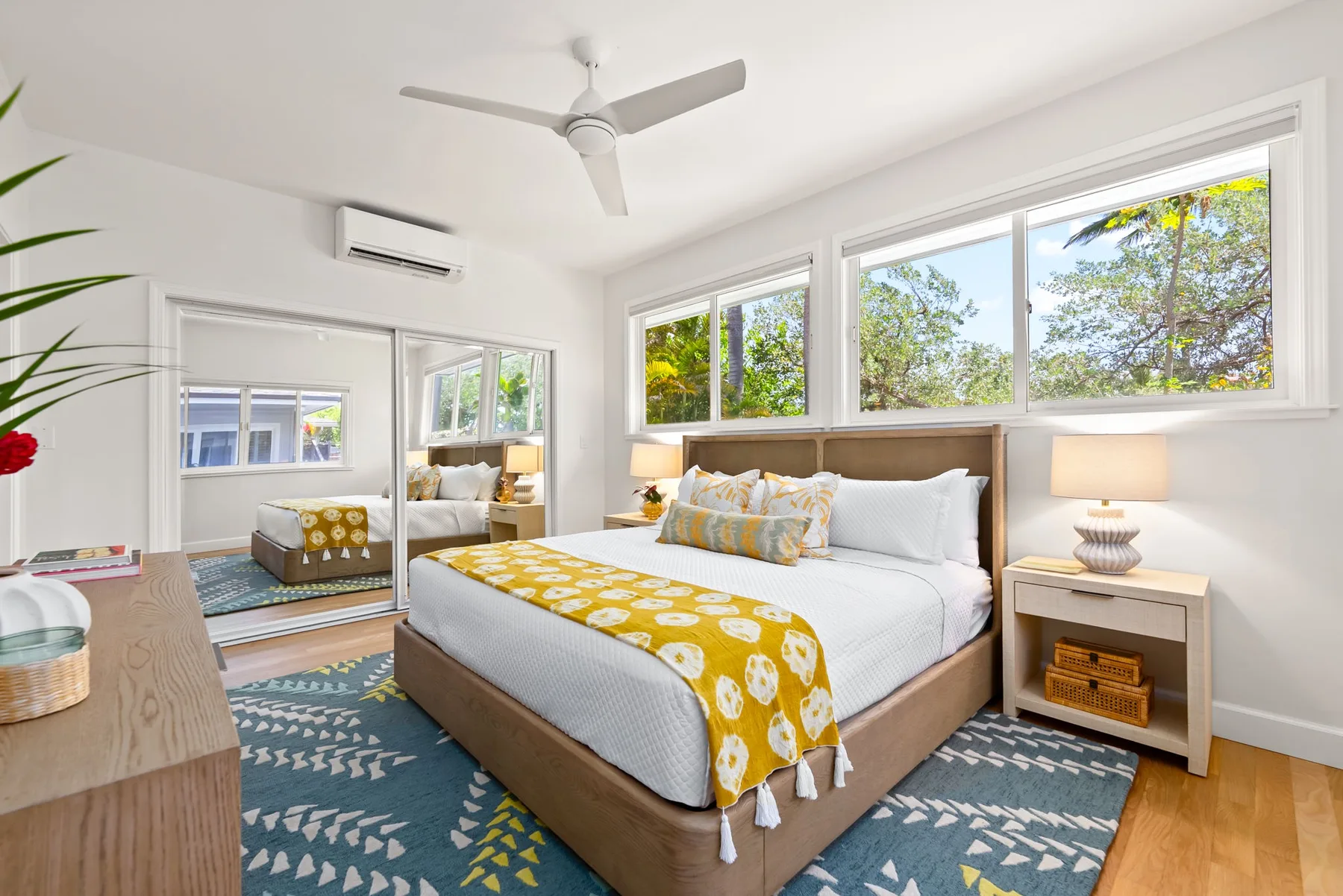 Un dormitorio luminoso con una cama bajo amplias ventanas con vistas a árboles frondosos.