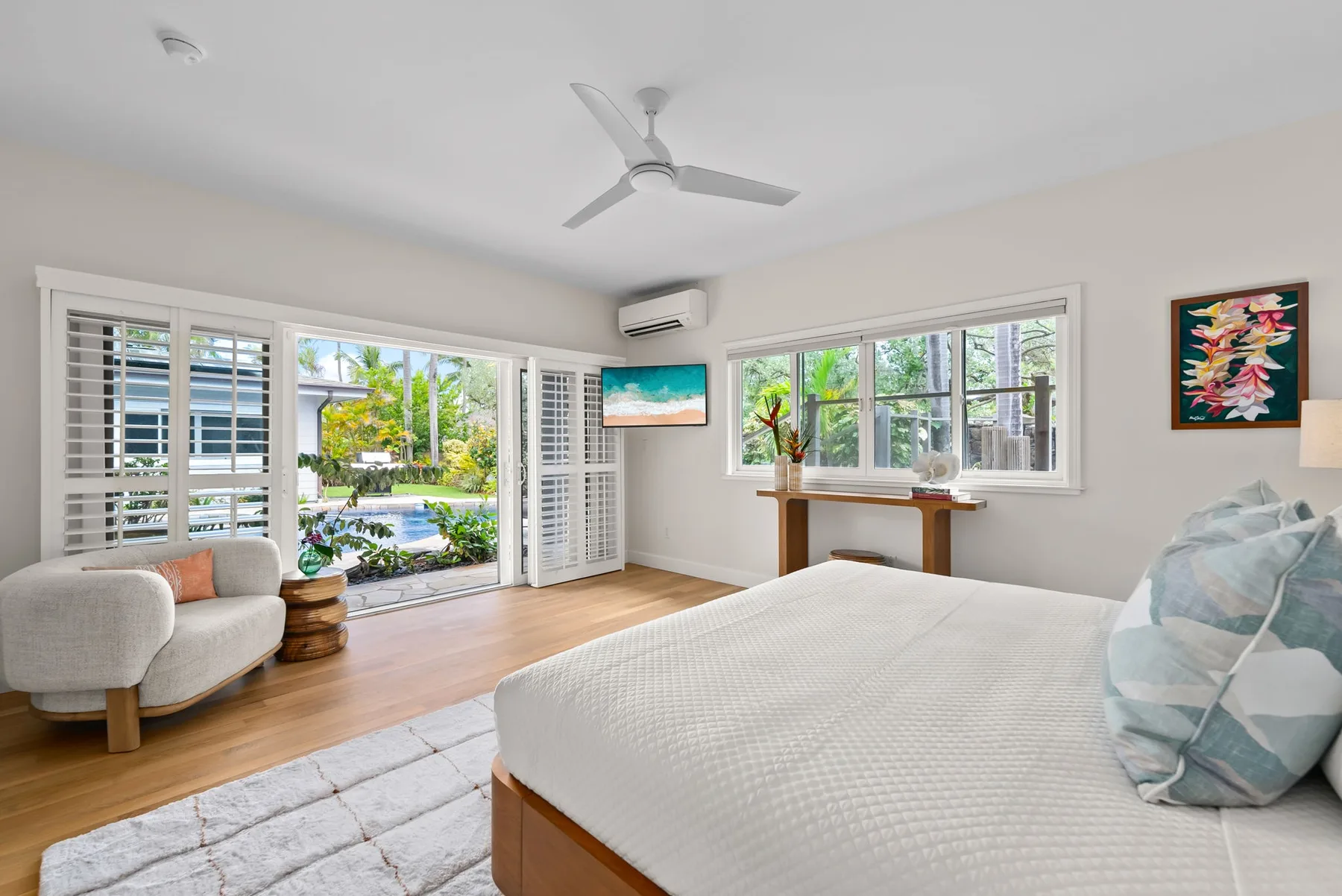 Un dormitorio luminoso con cama, asientos y ventanas con vistas a la vegetación.