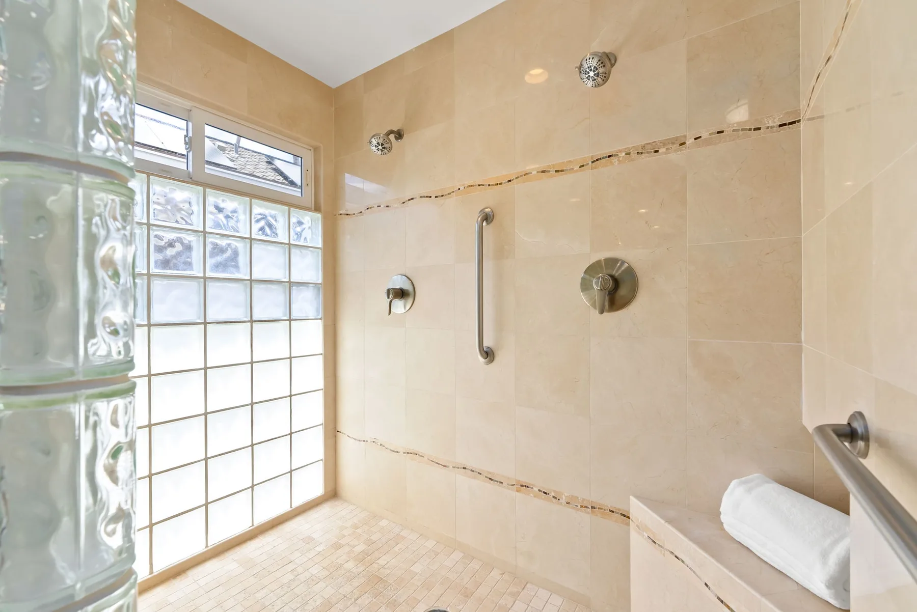 Una zona de ducha con azulejos, una ventana de bloques de vidrio y accesorios metálicos.