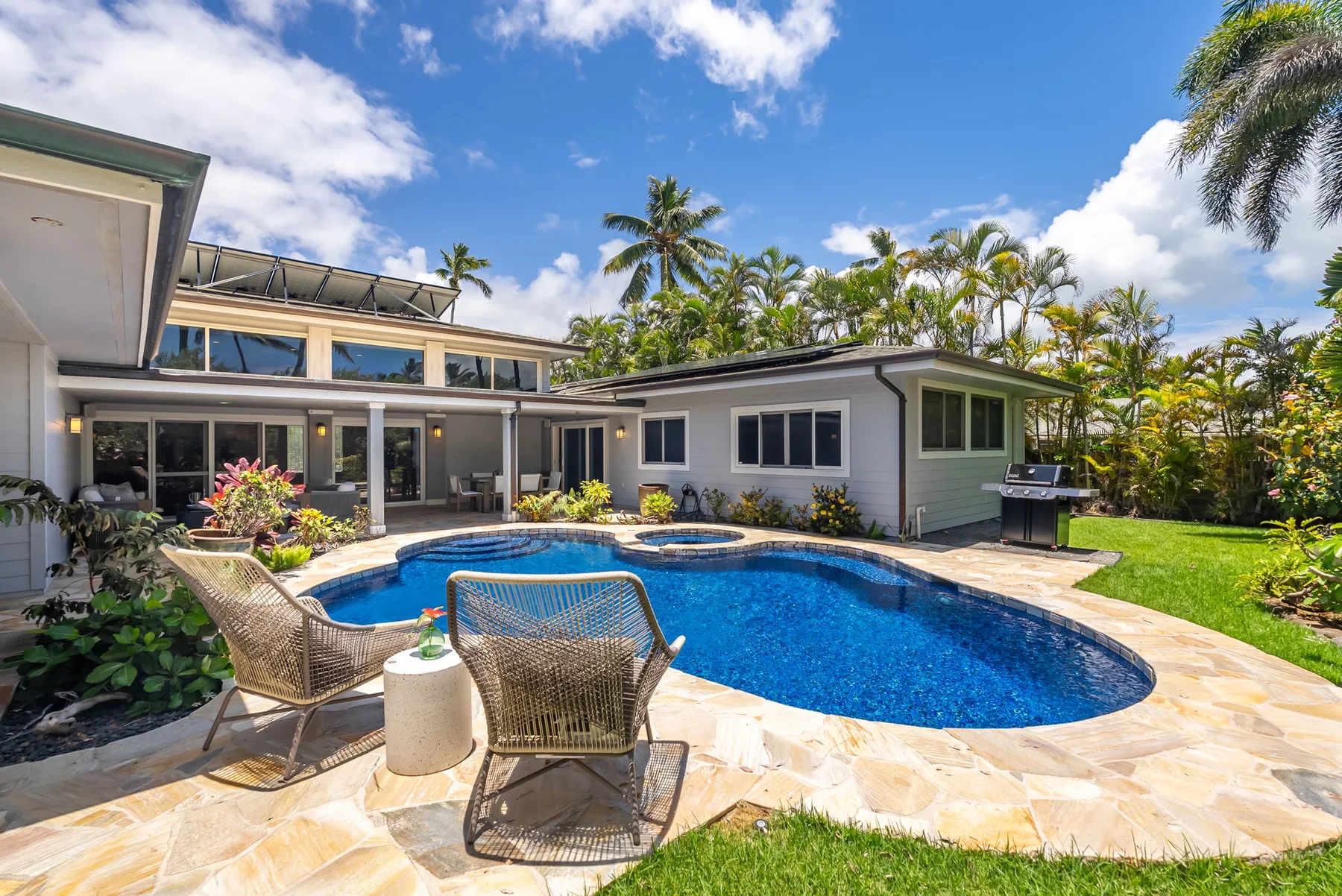 Un patio soleado rodea una piscina azul junto a una casa moderna.